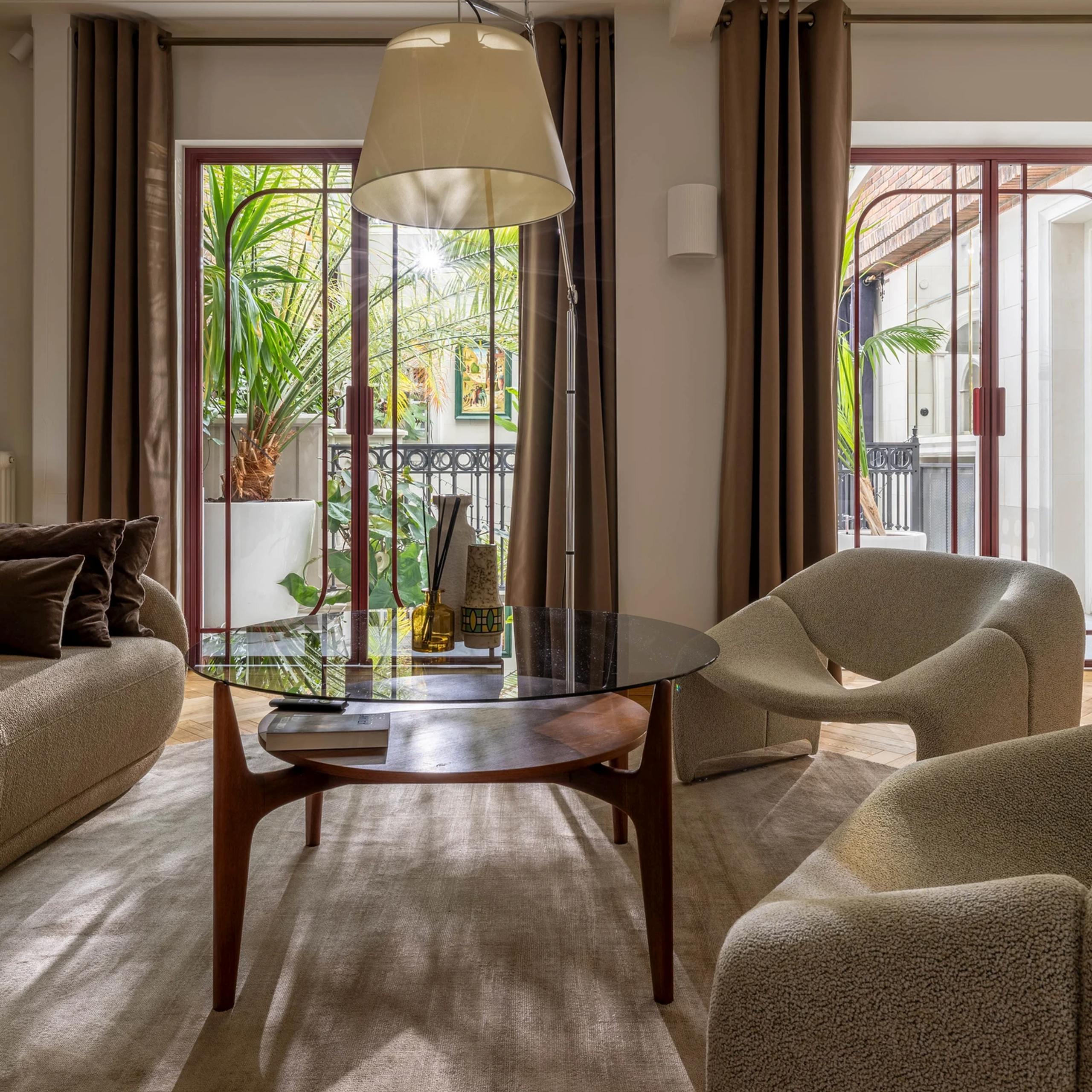 Elegancka lokalizacja do sesji biznesowych i rodzinnych – beżowa sofa, szklany stolik i duże okna z tropikalnym widokiem.