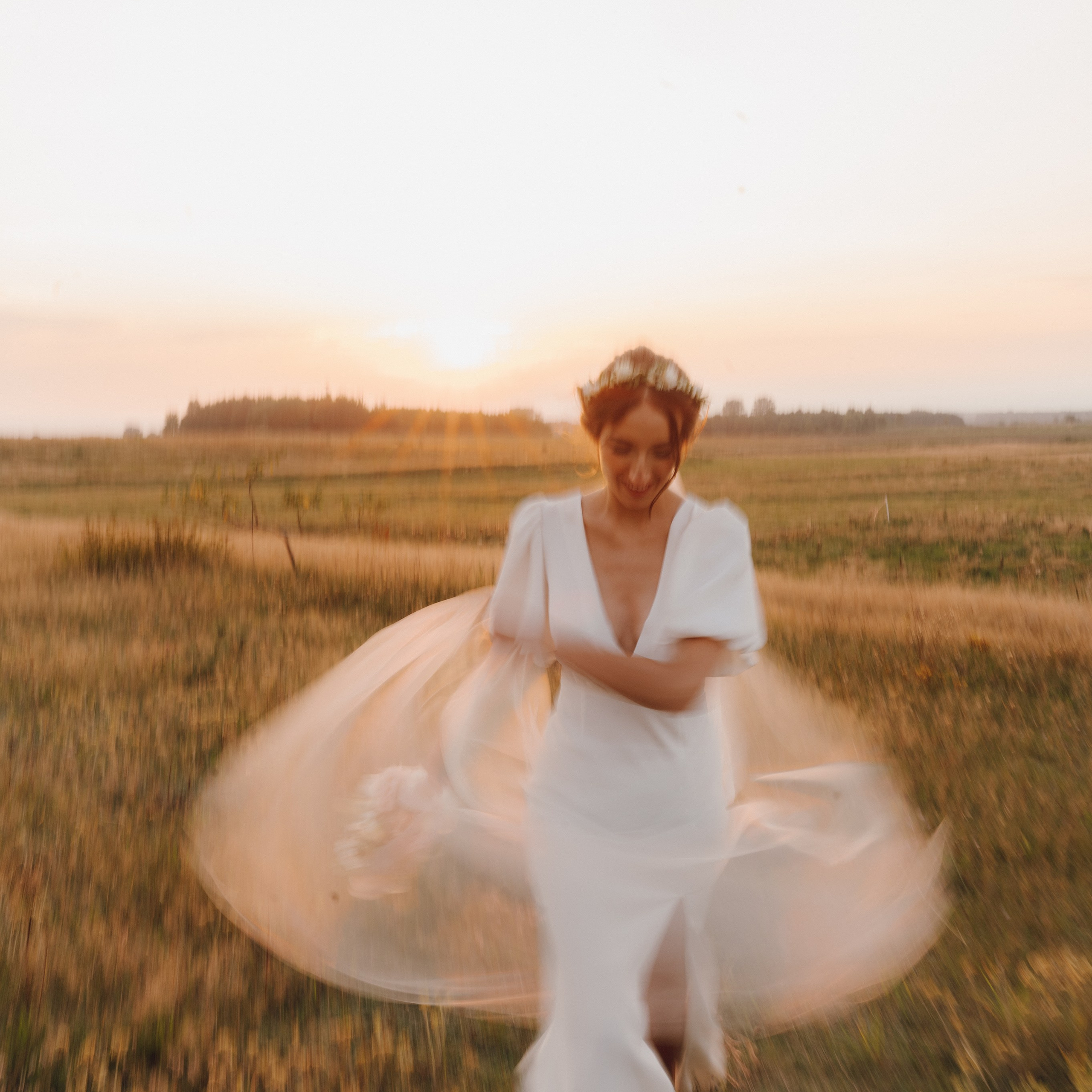 Panna młoda tańcząca na łące o zachodzie słońca – radość i lekkość w dniu ślubu.