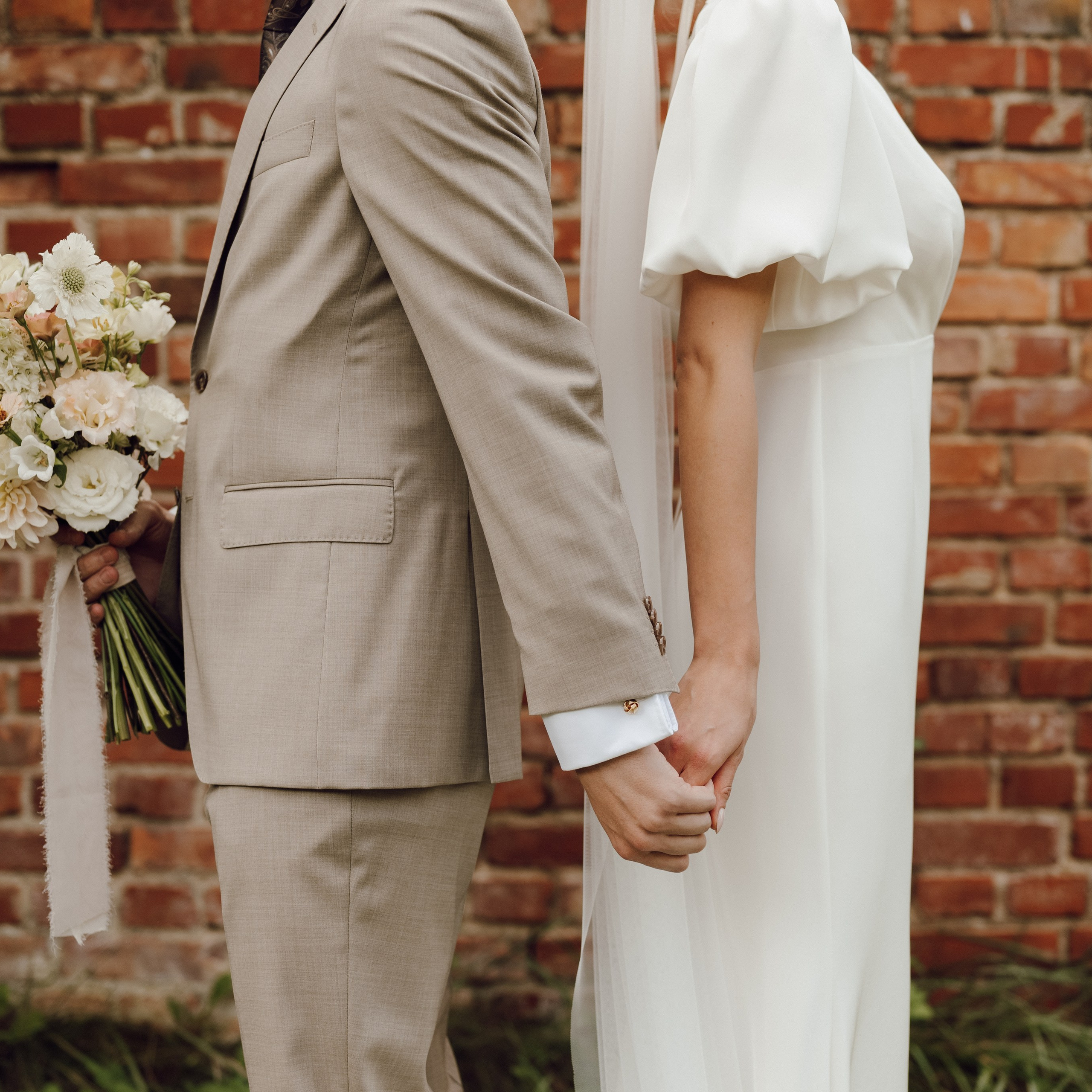 Para młoda trzymająca się za ręce przy ceglanej ścianie – romantyczna sesja ślubna w Poznaniu.