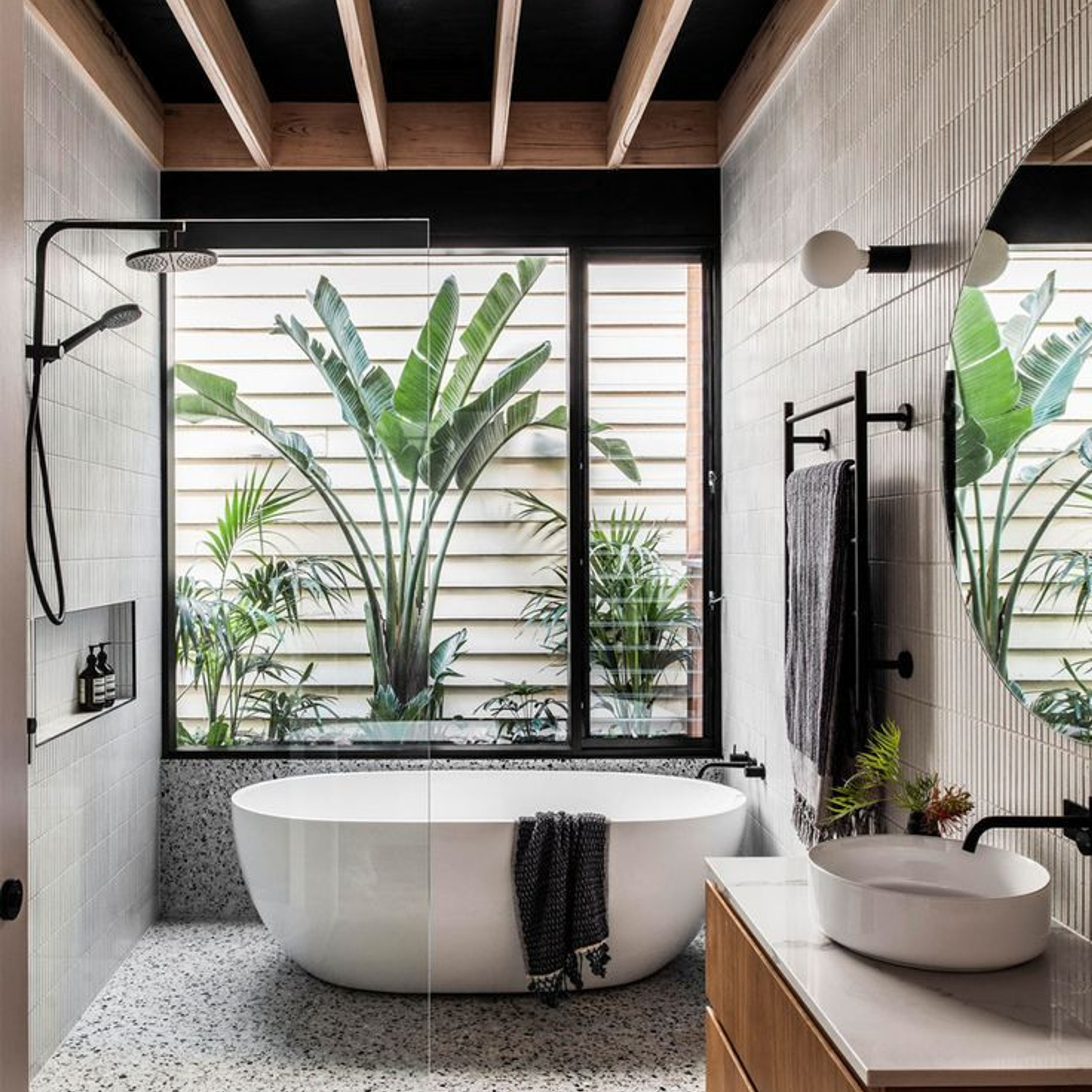 Elegant bathroom design with tropical outdoor views, featuring a freestanding bathtub, exposed wooden beams, black hardware, and a floating vanity with a vessel sink