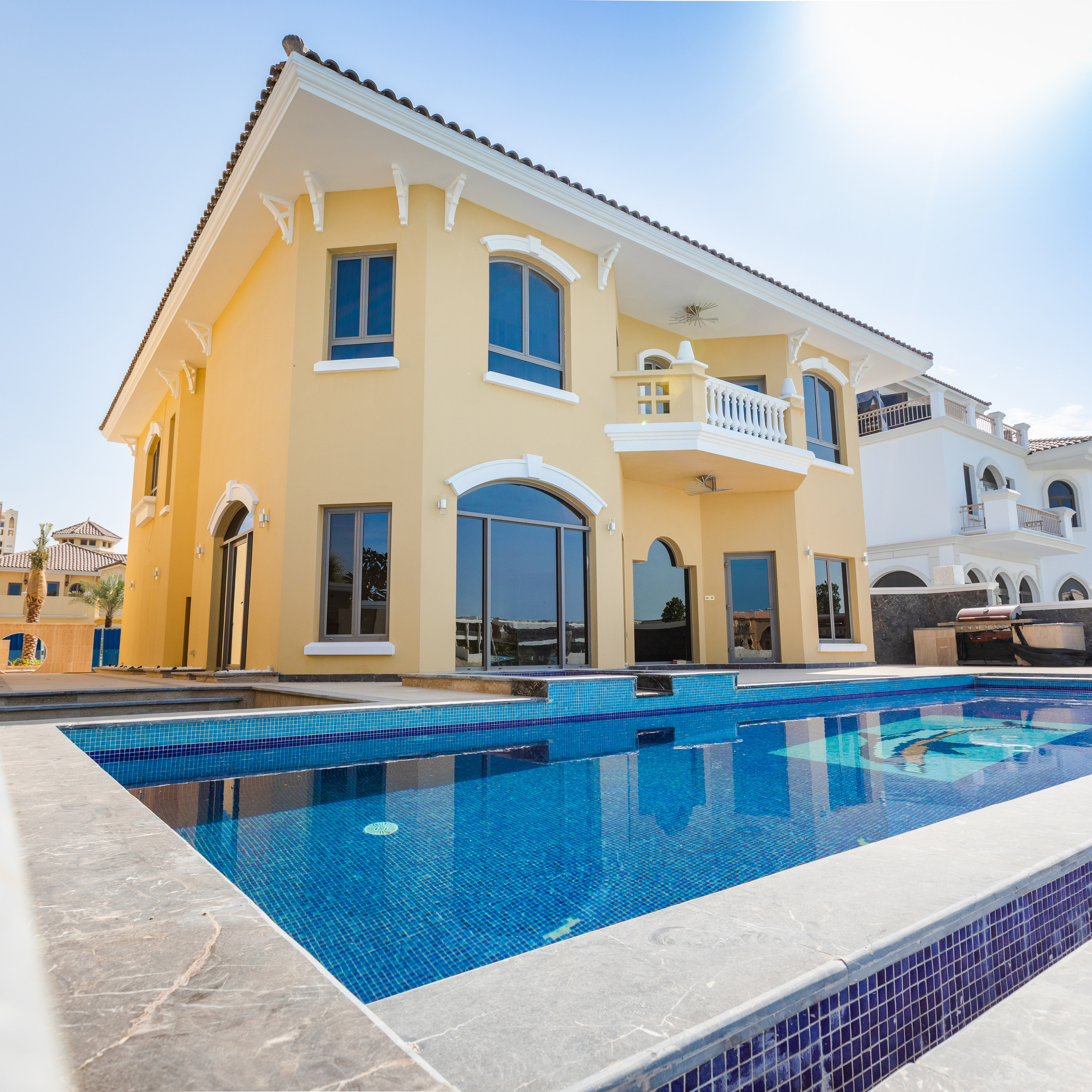 Charming Mediterranean-style villa with an expansive pool, showcasing beautiful arched windows, a balcony, and a bright yellow exterior