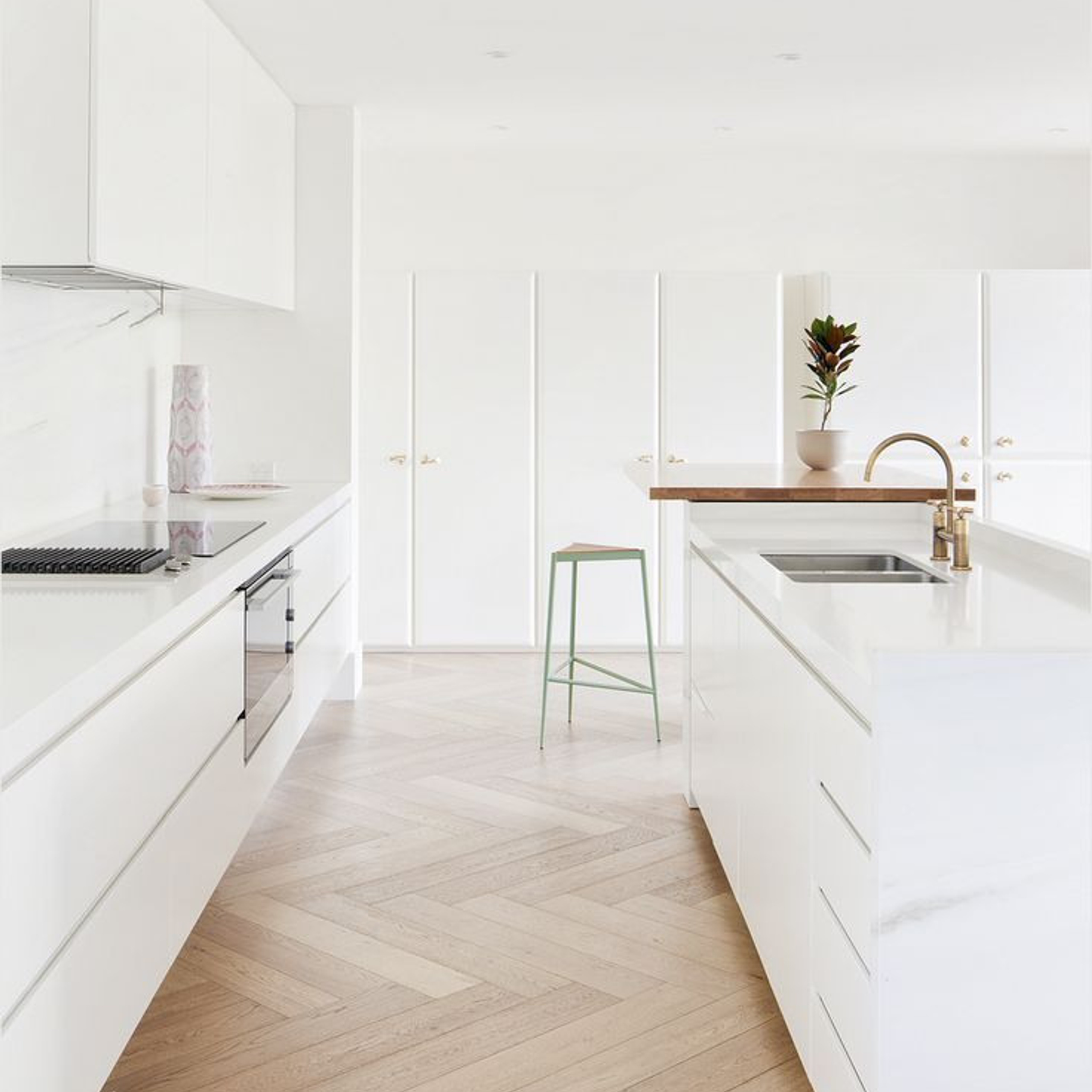 Bright, minimalist kitchen with all-white cabinetry, a marble island, and light herringbone wooden floors