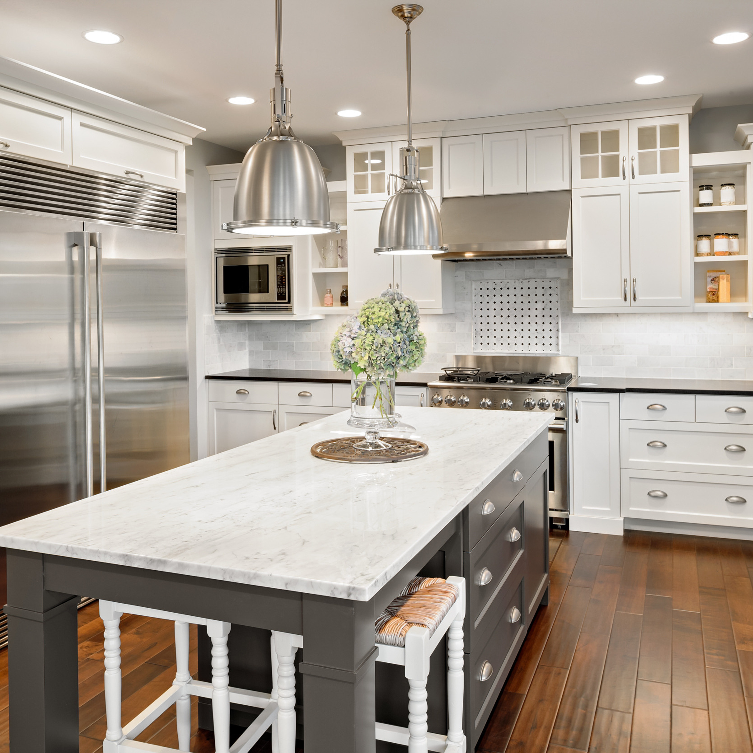 Spacious kitchen featuring white cabinets, large stainless refrigerator, and hanging pendant lights