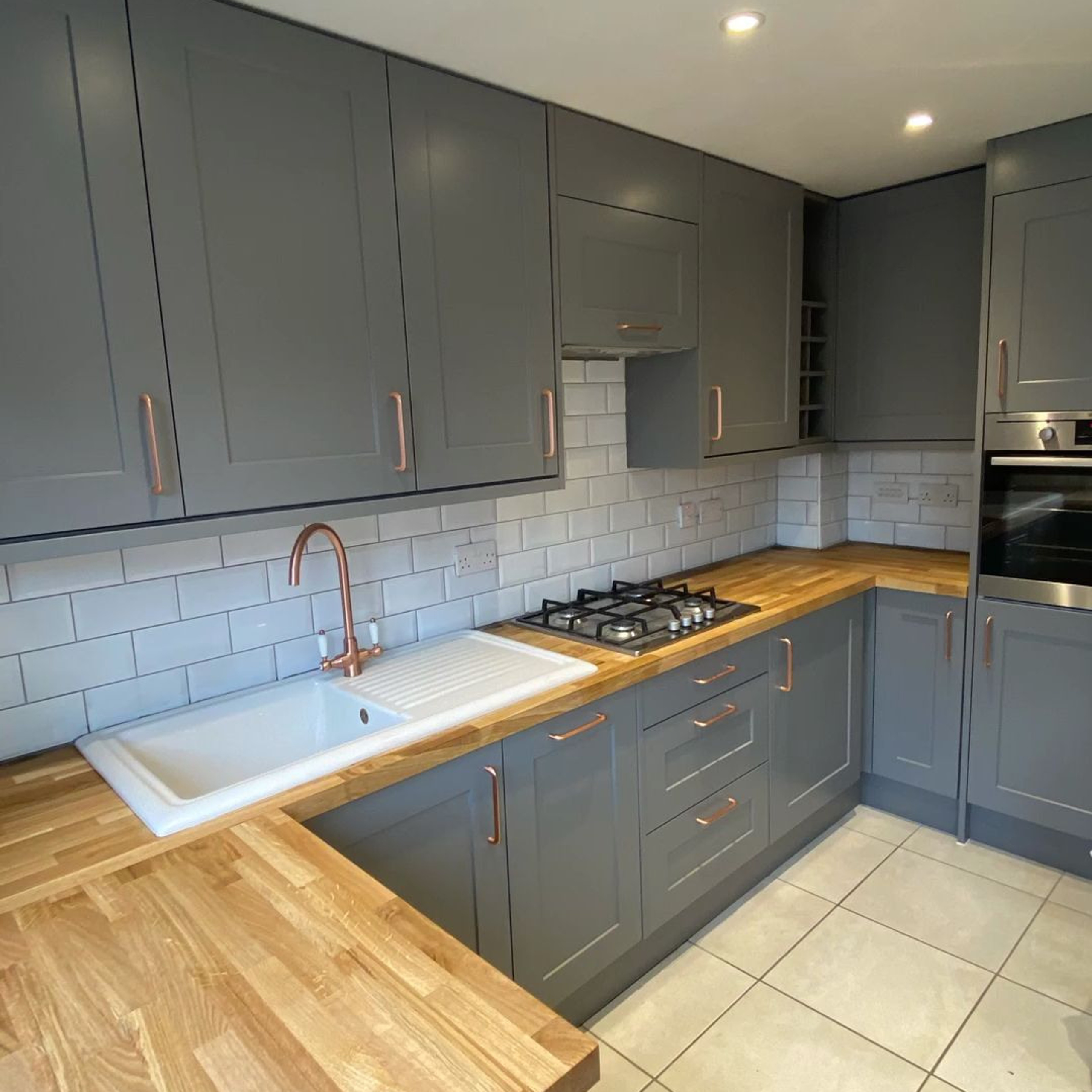 Contemporary kitchen with grey cabinets, copper handles, wooden countertops, and a white subway tile backsplash, featuring an integrated gas stovetop and a copper faucet