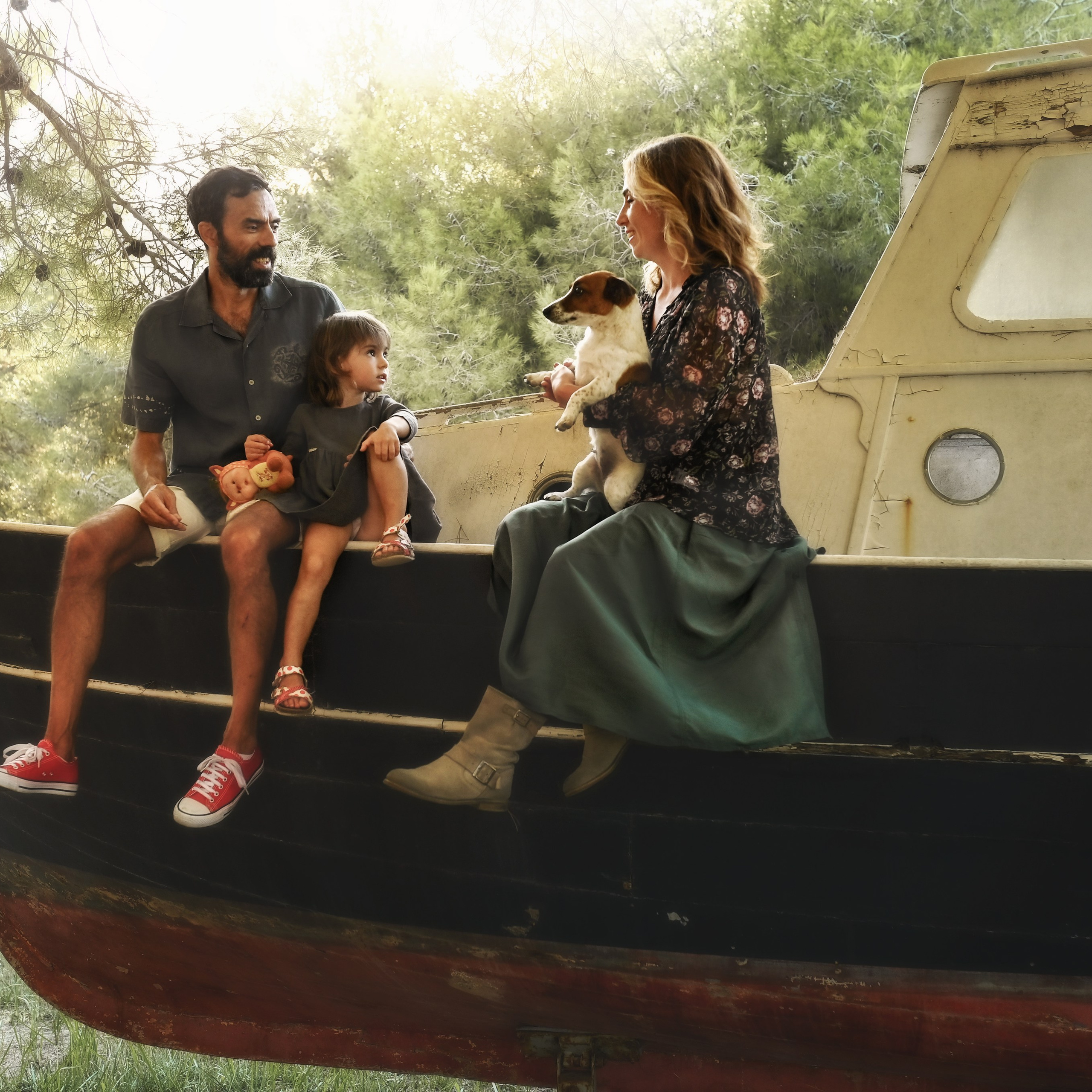  A family with a child and a dog sitting on an old boat in a pine forest, enjoying the golden morning light.