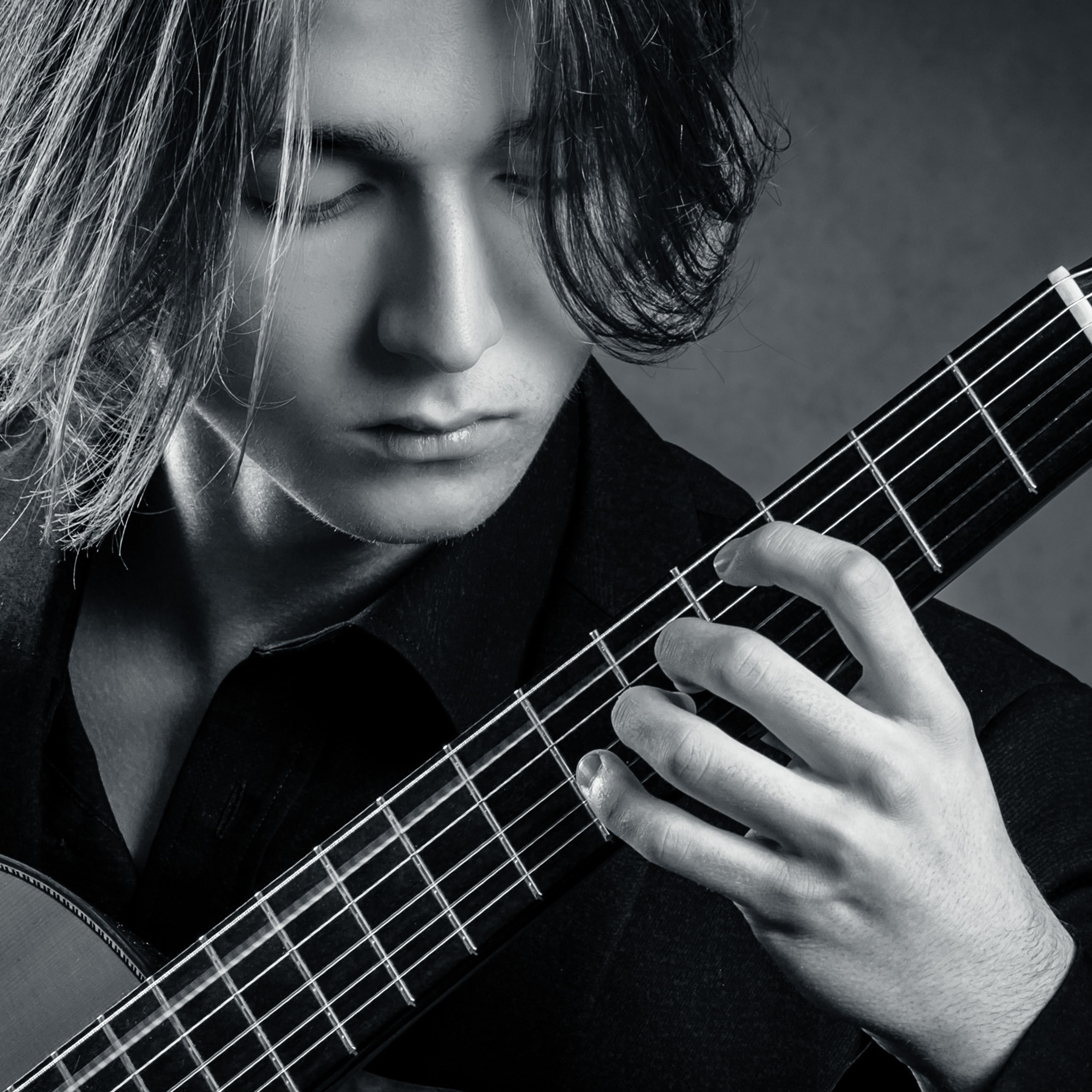 Ein Nahaufnahme-Porträt eines jungen, langhaarigen Gitarristen während des Spielens mit Fokus auf seiner linken Hand am Gitarrenhals.