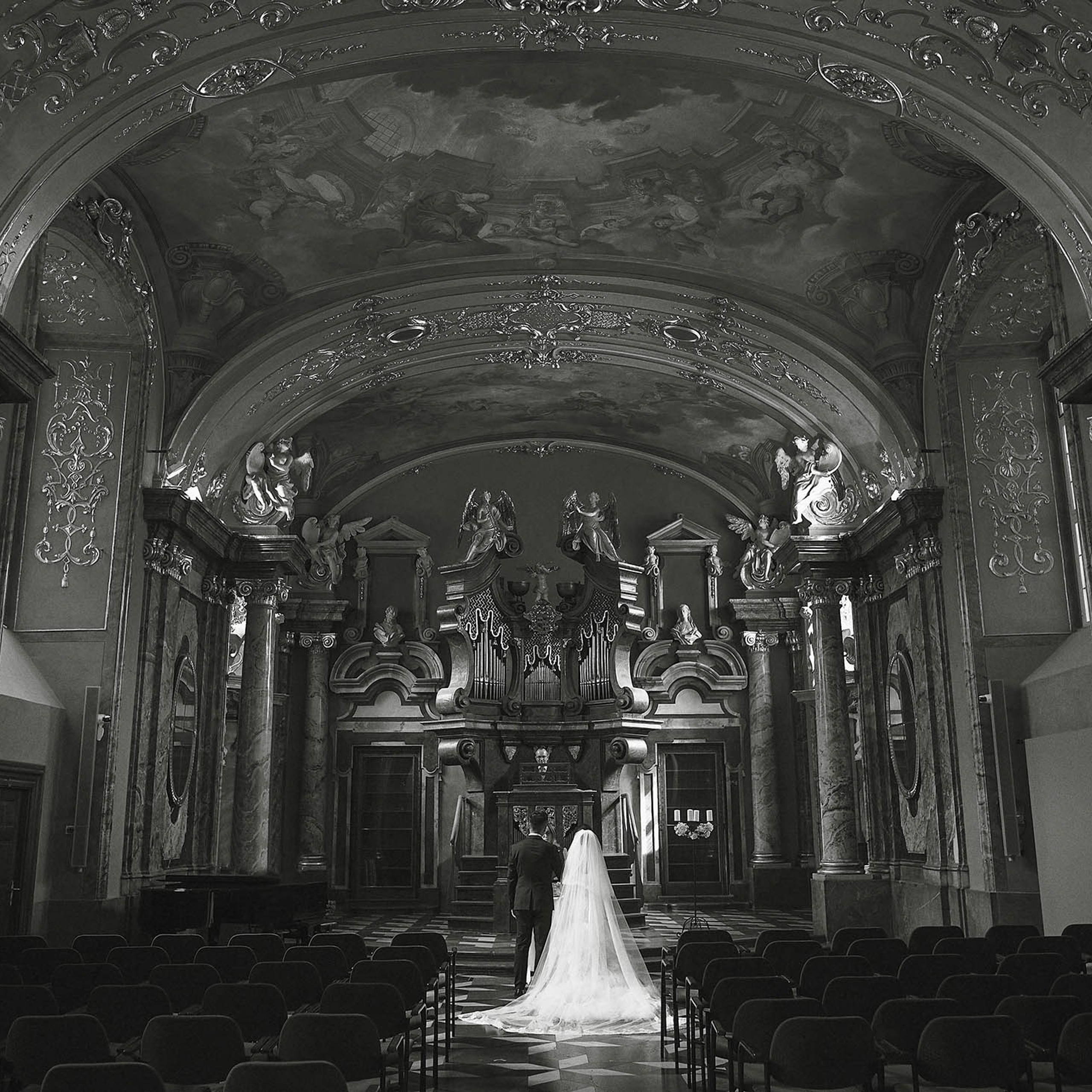A view from the back looking towards the altar where a young bride and groom from China are exchanging vows at the Klementinum Mirror Chapel in Prague