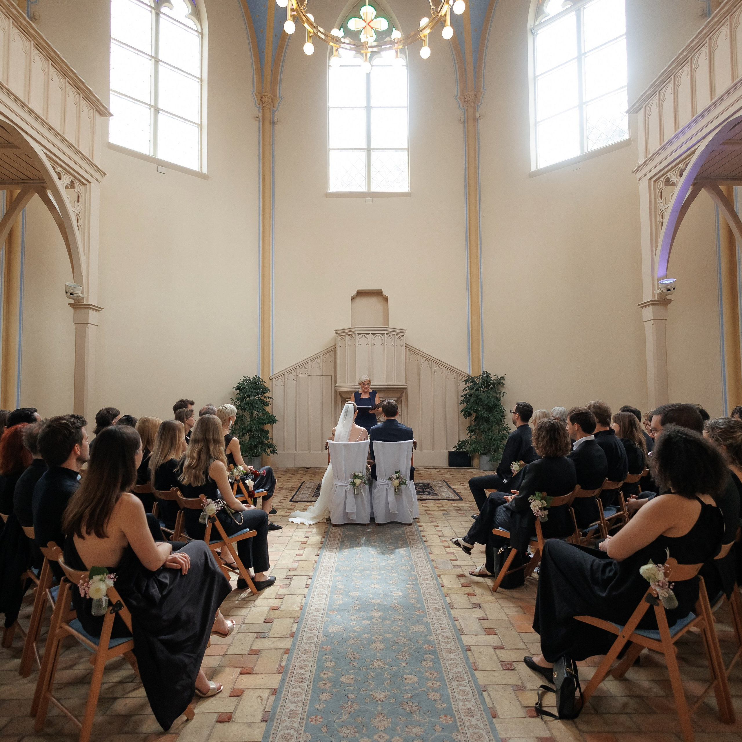 Brautpaar während der standesamtlichen Trauung im Innenraum der Alten Neuendorfer Kirche, umgeben von den Hochzeitsgästen