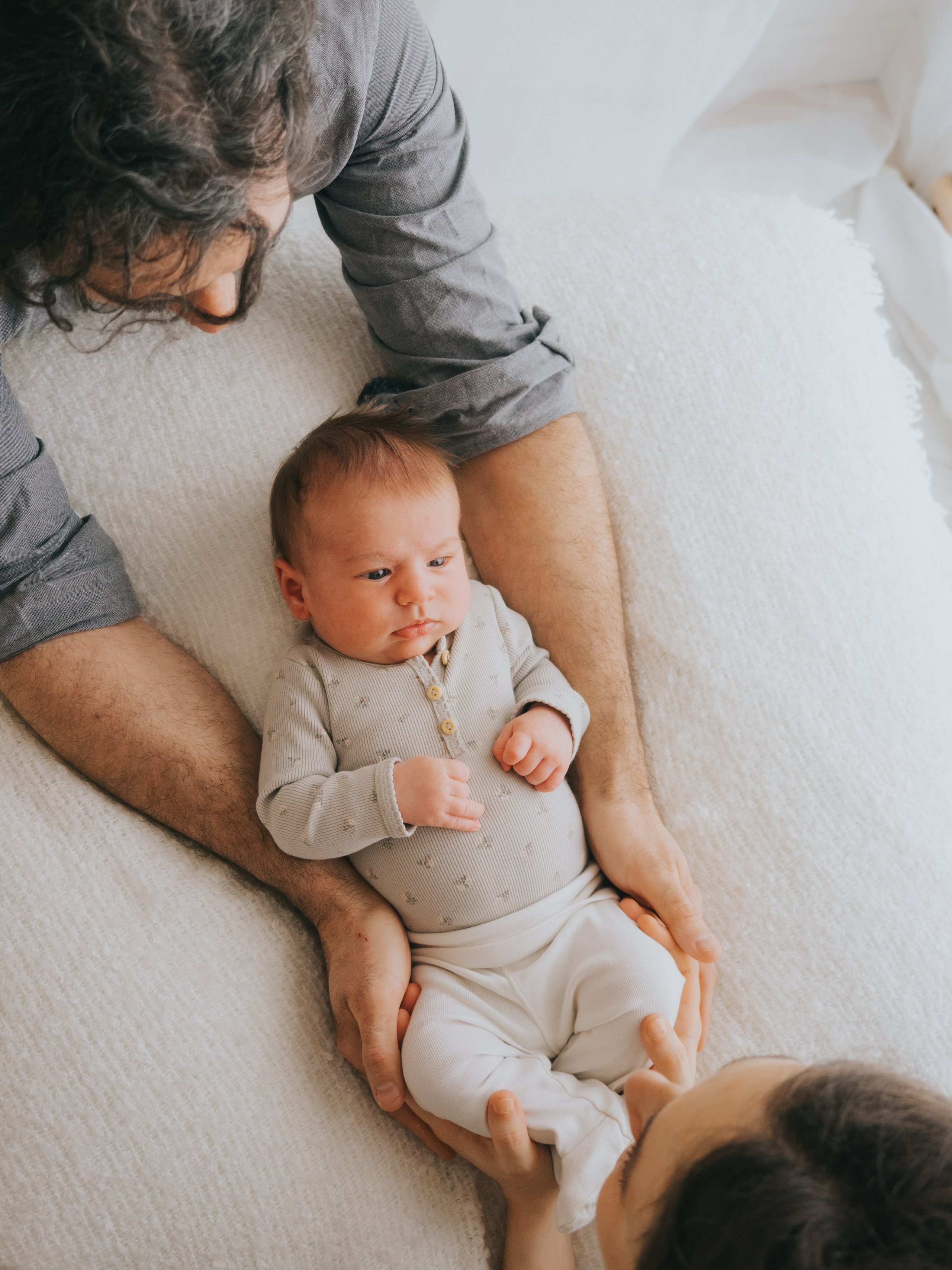 Newborn looking at their parents holding her.