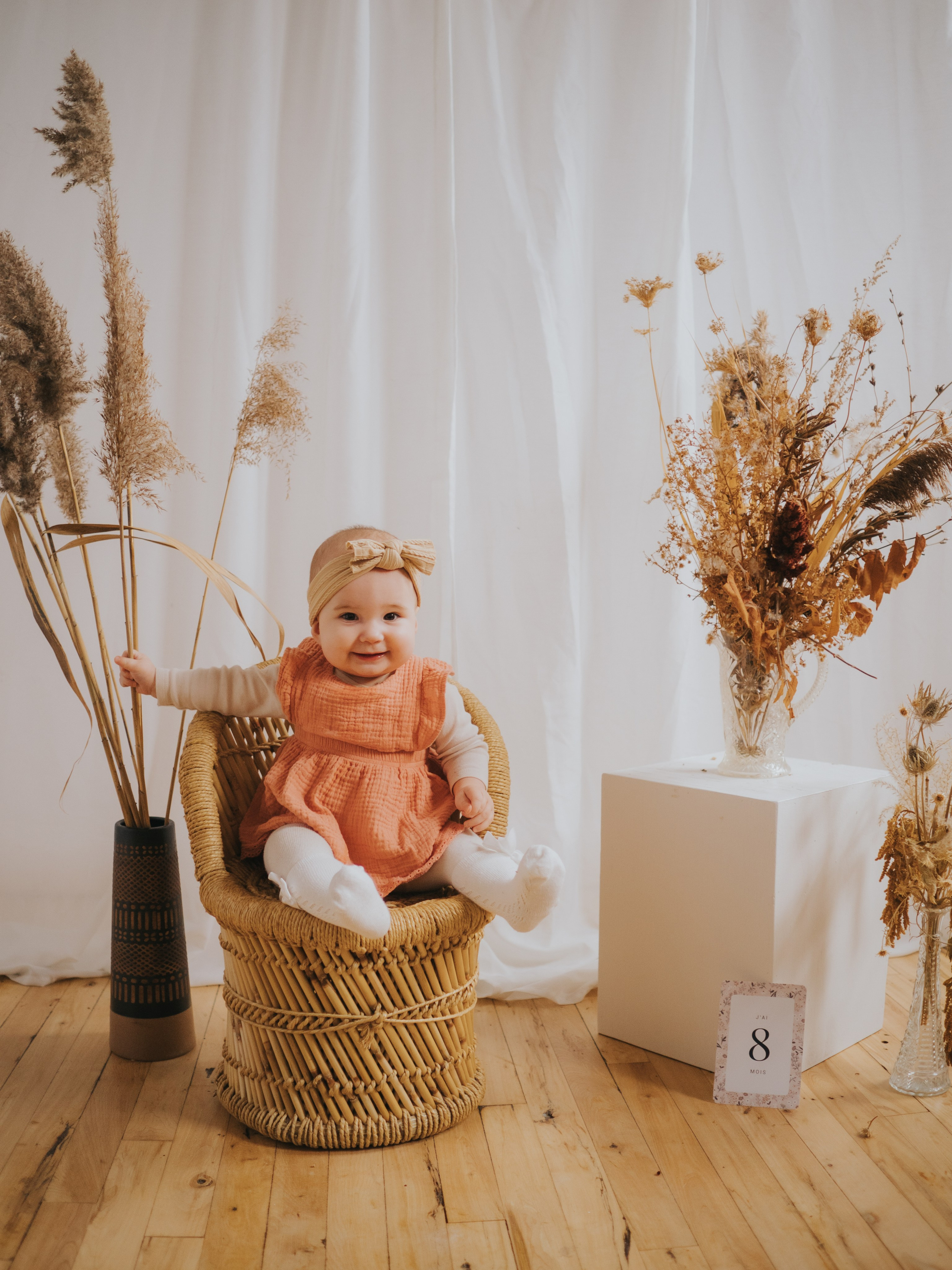 Baby sitting on rattan chair with 8 months milestone card next to her.