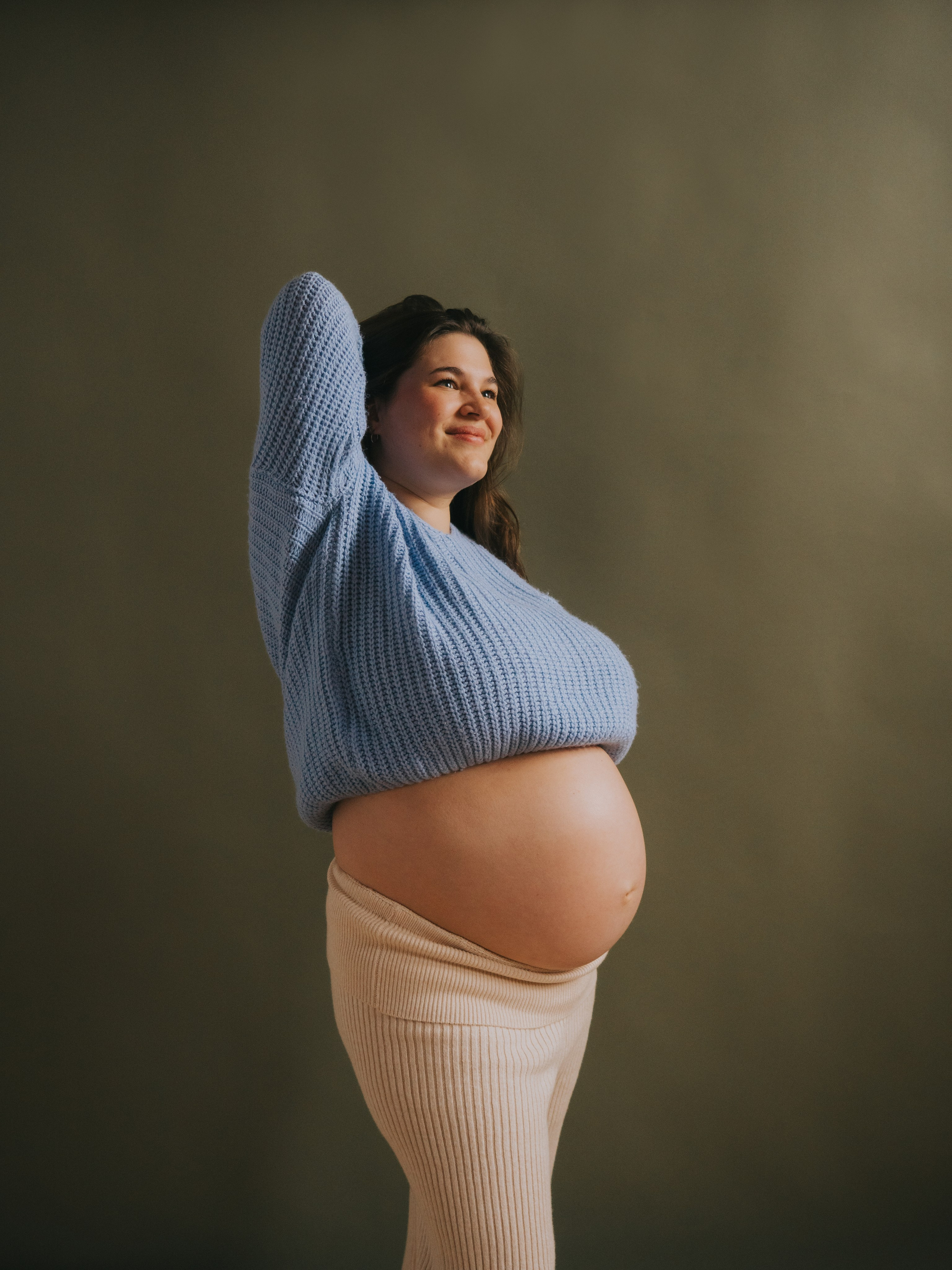 Pregnant woman standing in front of green backdrop.
