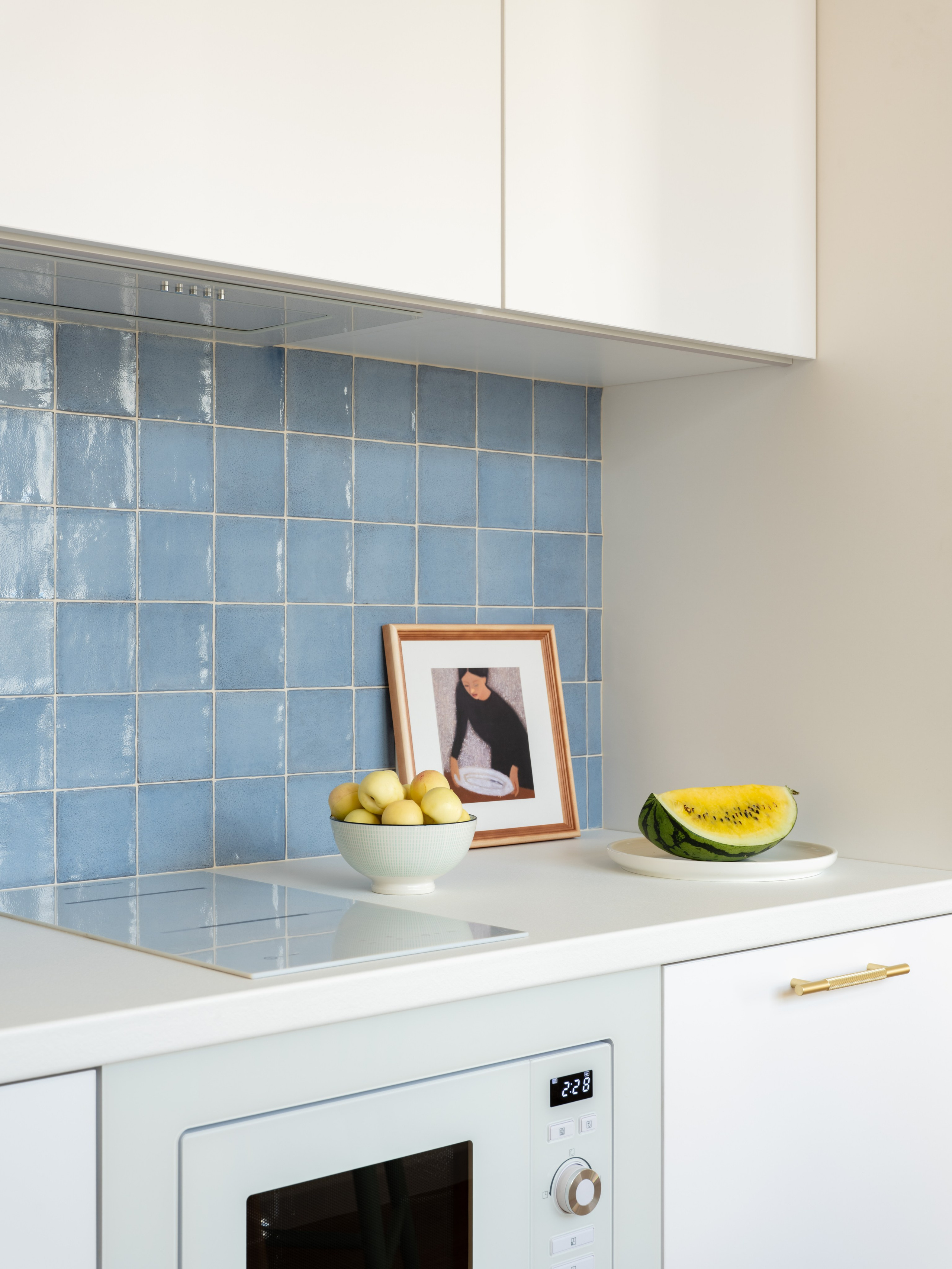 Голубой фартук на белой кухне с деревянными стульями.