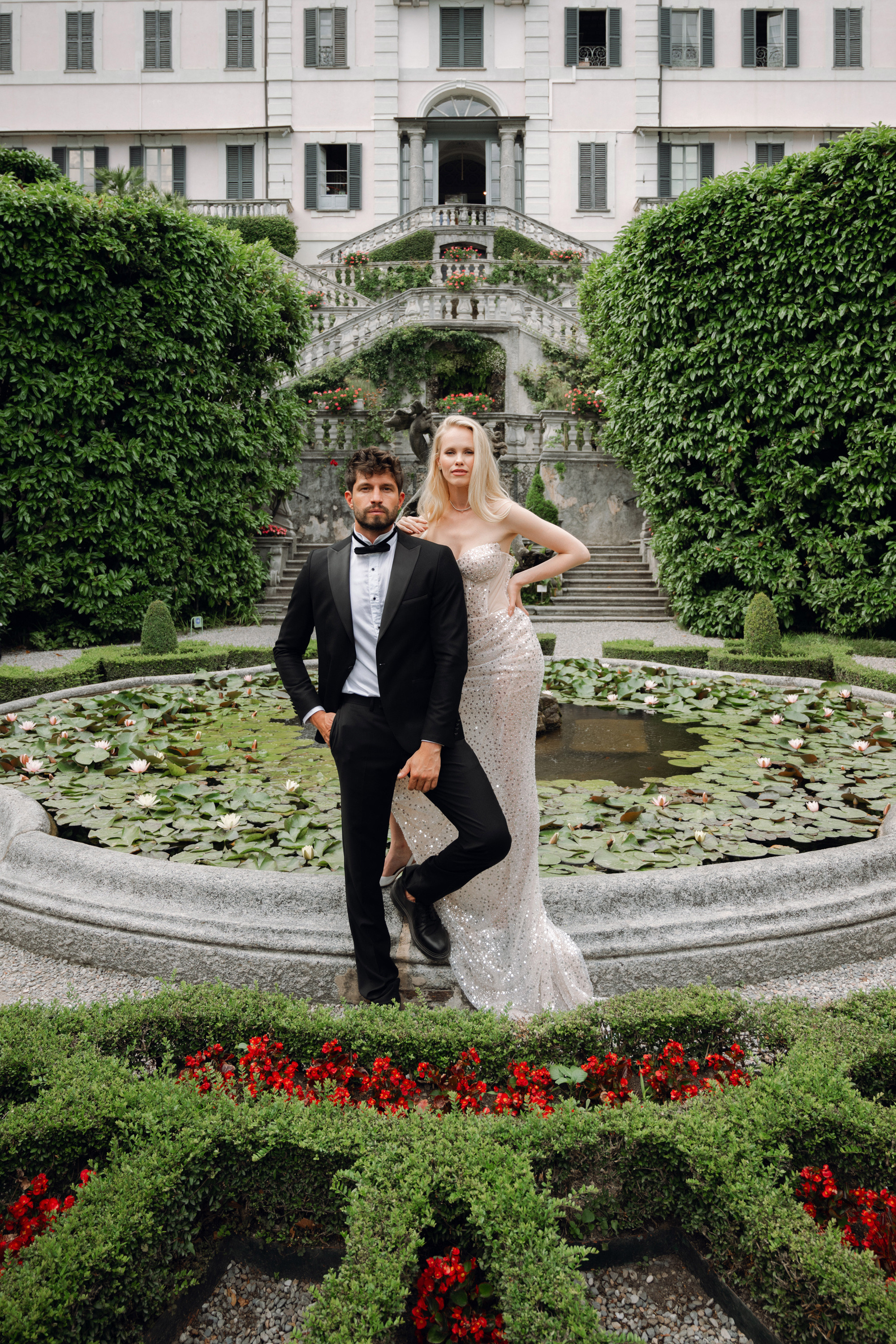 a bride and groom pose in front of a fountain