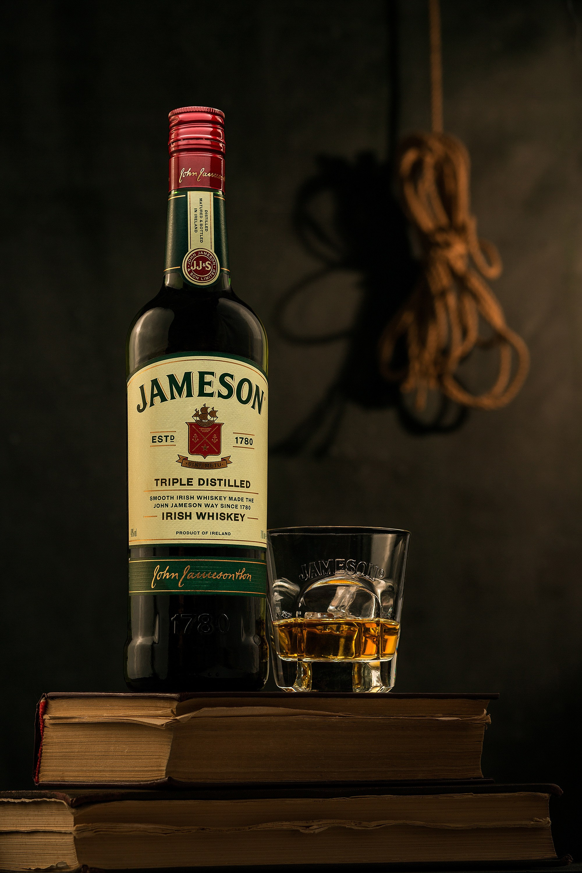 Rustik və maskulin mühitdə Jameson viskisi butulkası, yan tərəfdən yumşaq işıqlandırma, etiketdə dairəvi işıq və fonunda kənd ipi ilə birlikdə.