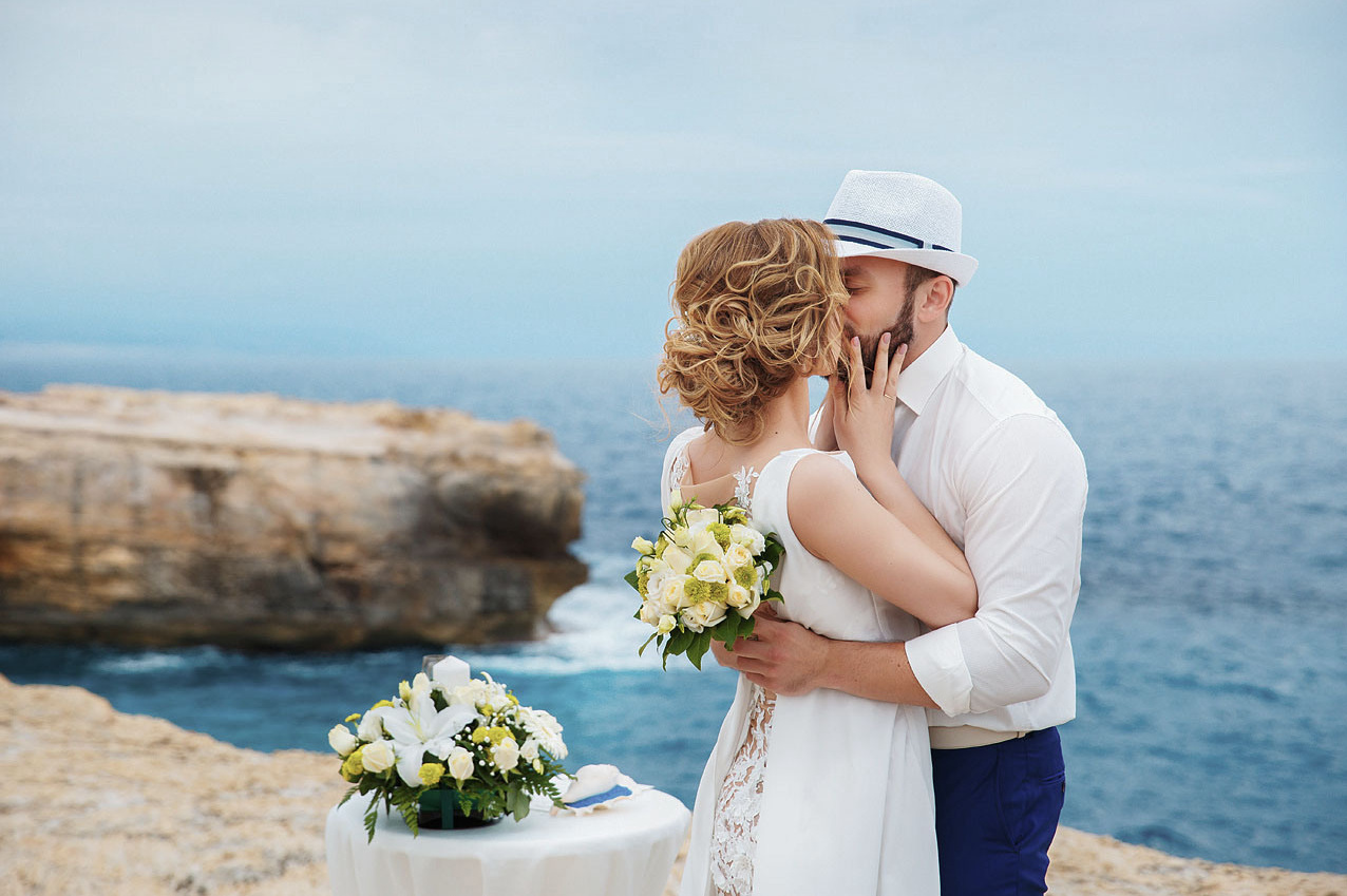 Молодожены целуются на свадебной церемонии на фоне моря на Крите. Фотограф, свадьба в Греции.