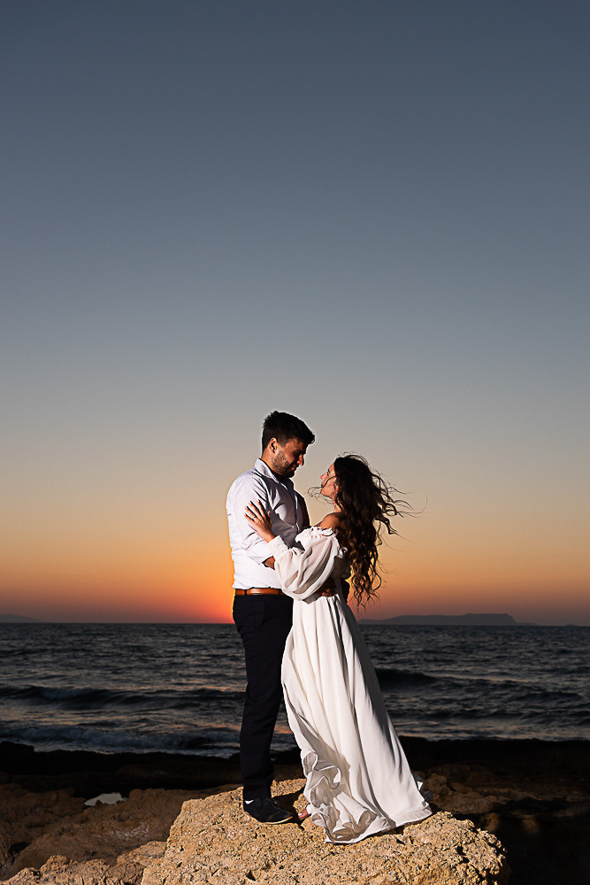 A couple of the bride and groom are hugging on the seashore at sunset