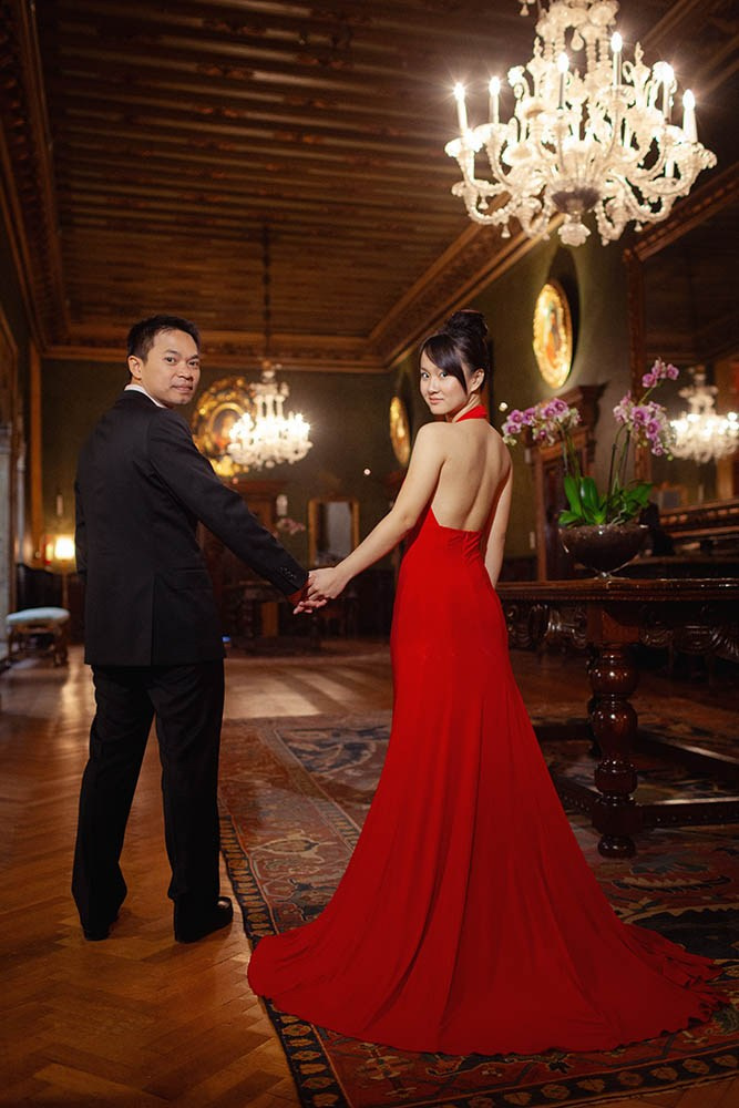 A stylishly dressed Thai couple look back towards the lens gaze as they stand in the historic parlor of the Hotel Danieli in Venice.