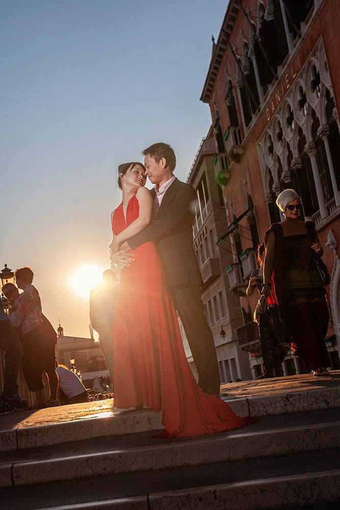 Thai couple embracing above the canal near Hotel Danieli in Venice as the sun flares from behind.