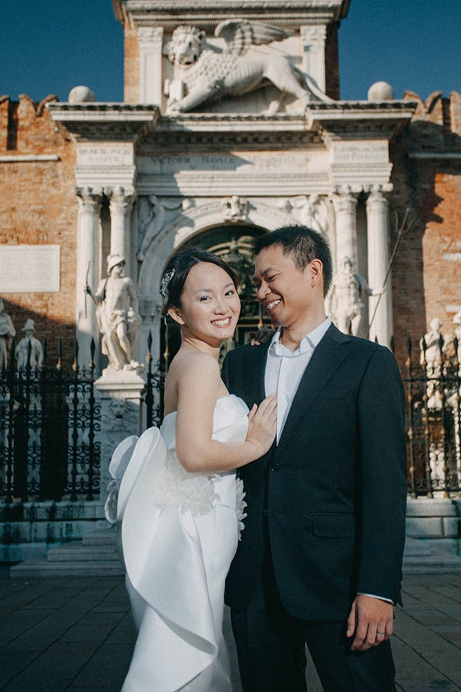 The bride smiles as the groom pulls her close near the historic entry to Arsenale in Venice.