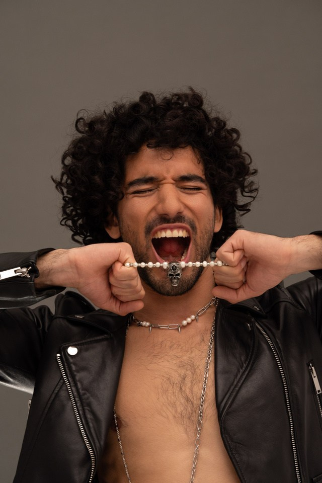Male model in a leather jacket wearing a silver chain, campaign shot on grey background