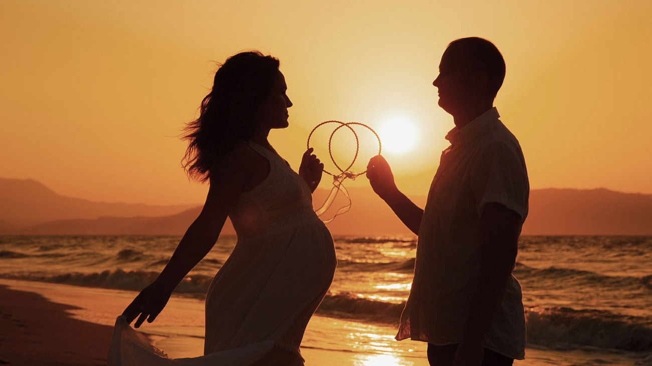 Молодожены на закате на пляже на Крите, держат в руках венки для венчания. Фотограф в Греции.