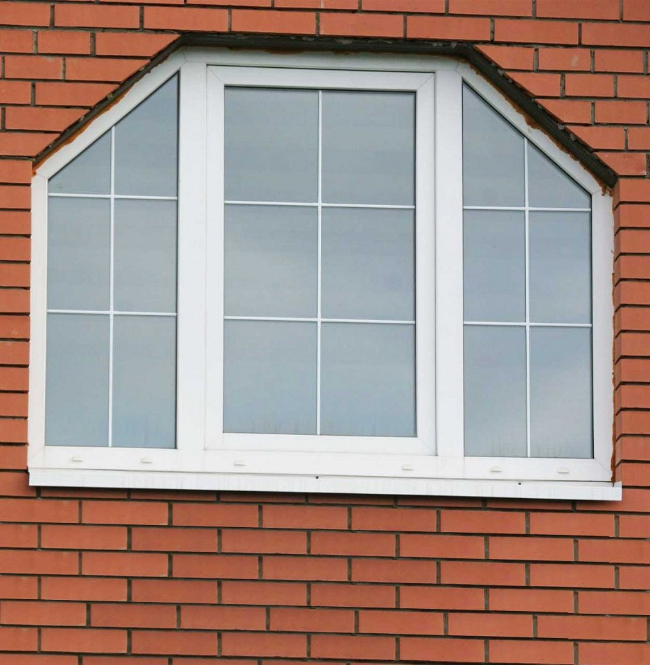 Белое, трапециевидное пластиковое окно, разделенное декоративными элементами - шпроссами.