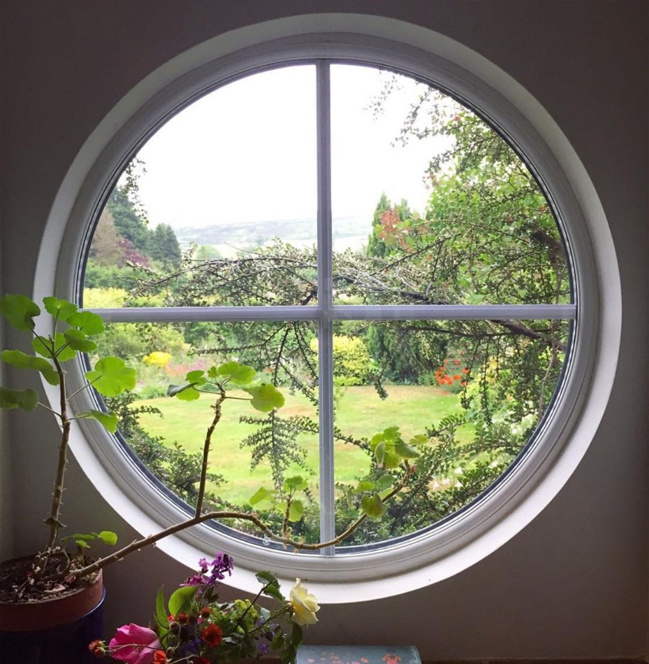 Круглое пластиковое окно белого цвета, разделенное вертикальным и горизонтальным фальш-переплетом.