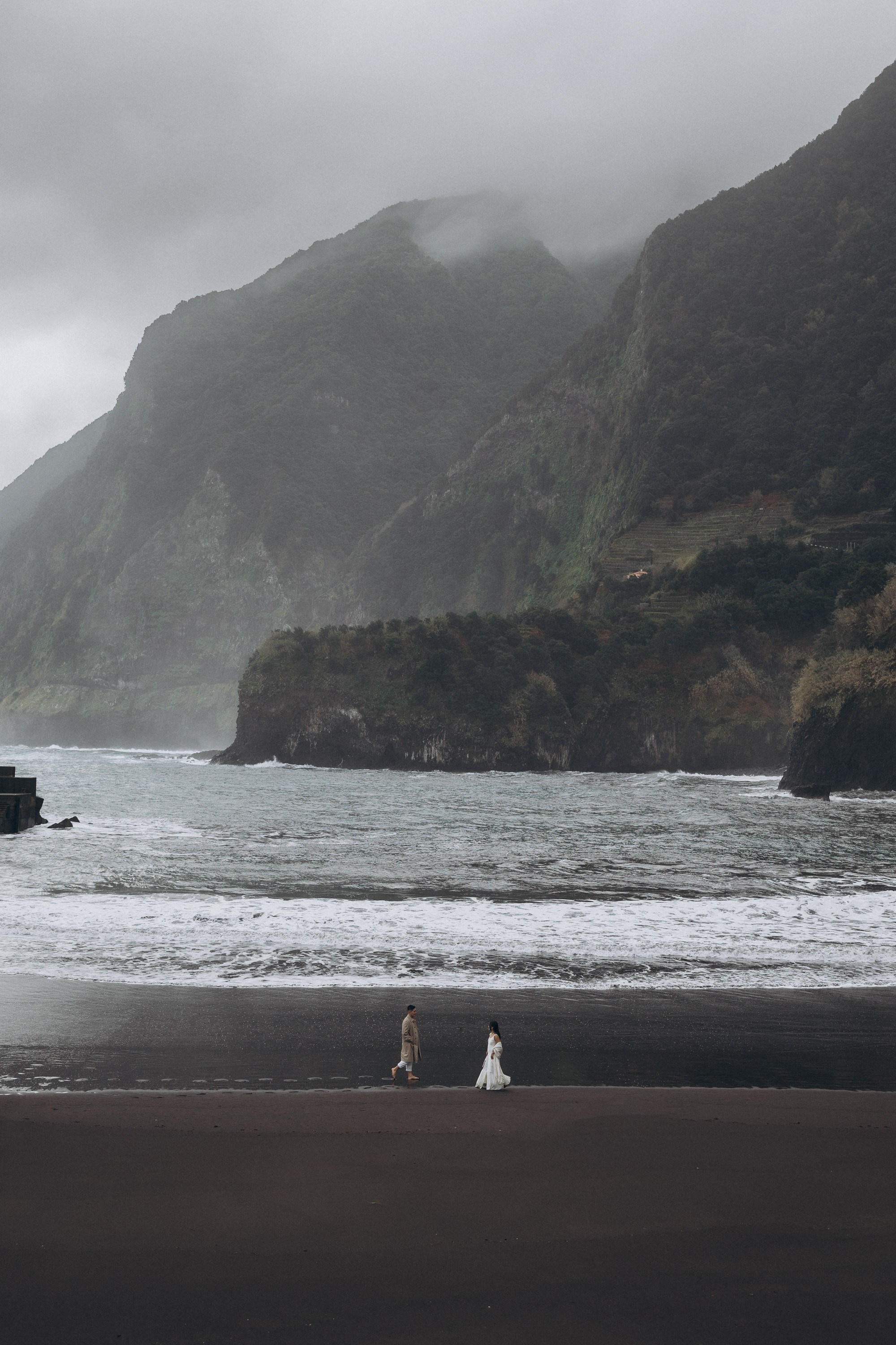 cinematic couple walking on Seixal black sand beach Madeira reflection ocean photo