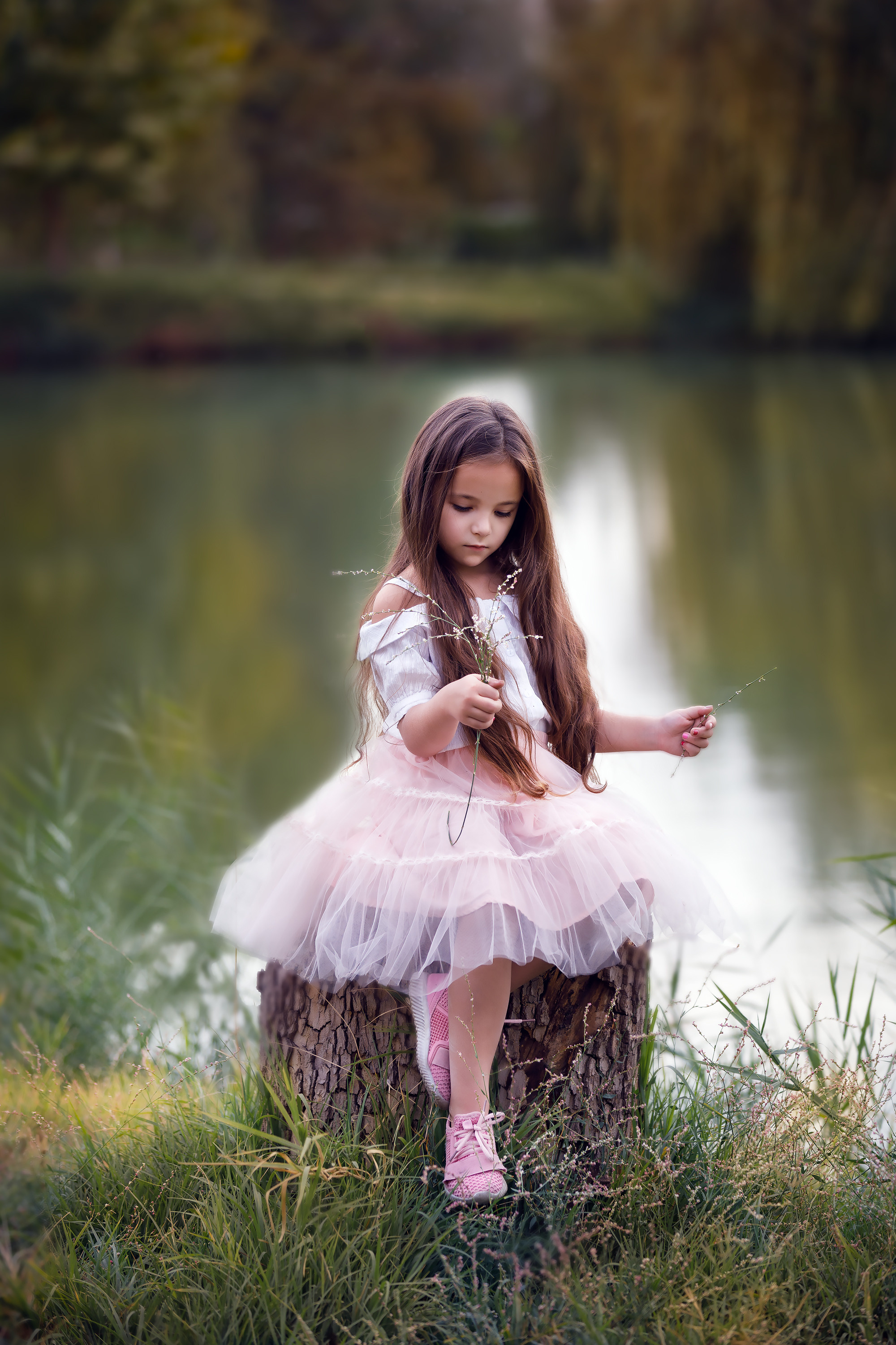 Маленькая красивая девочка с очень длинными распущенными волосами в розовой одежде на берегу озера