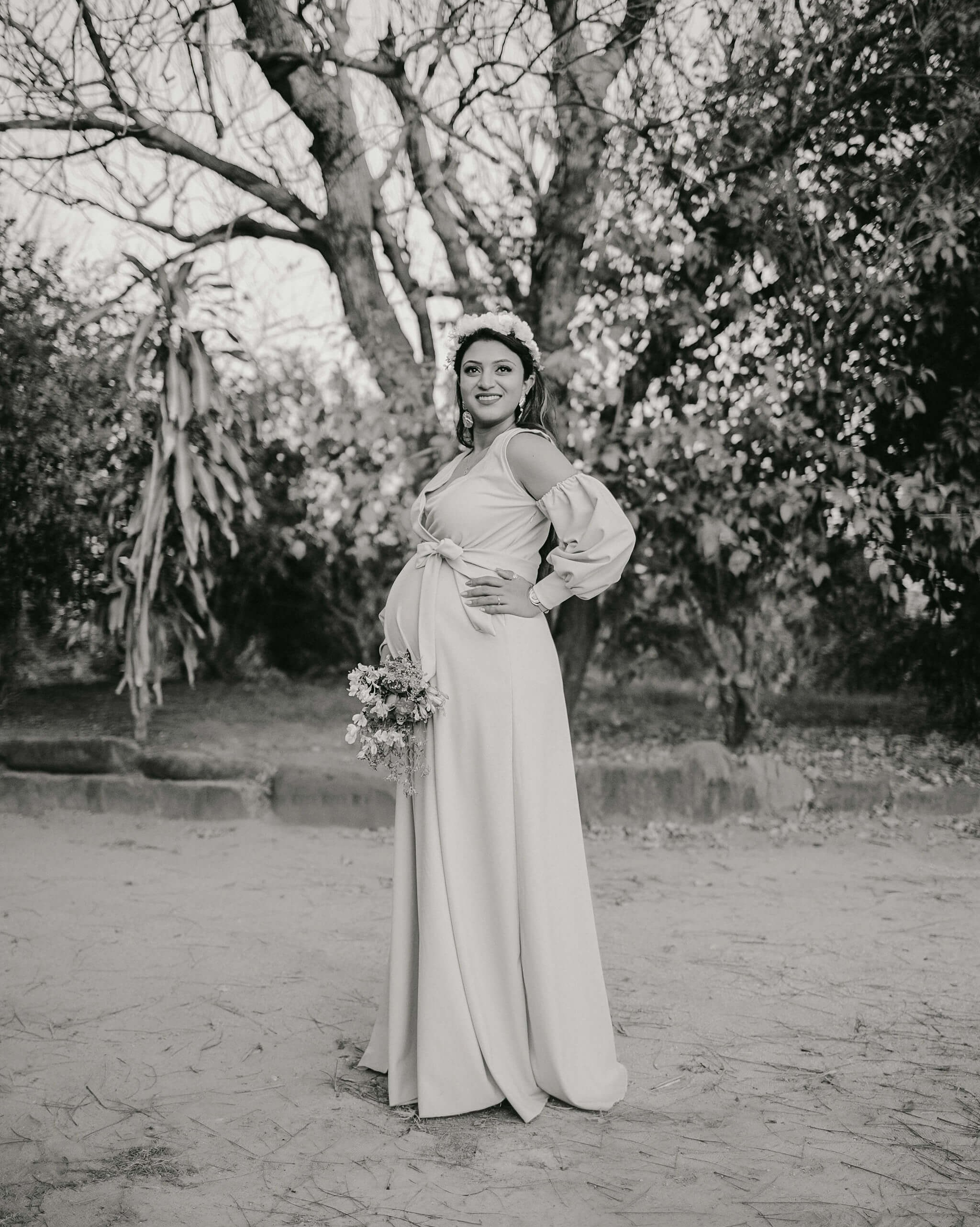 Kenya coast maternity shoot, woman softly smiling in natural garden setting.