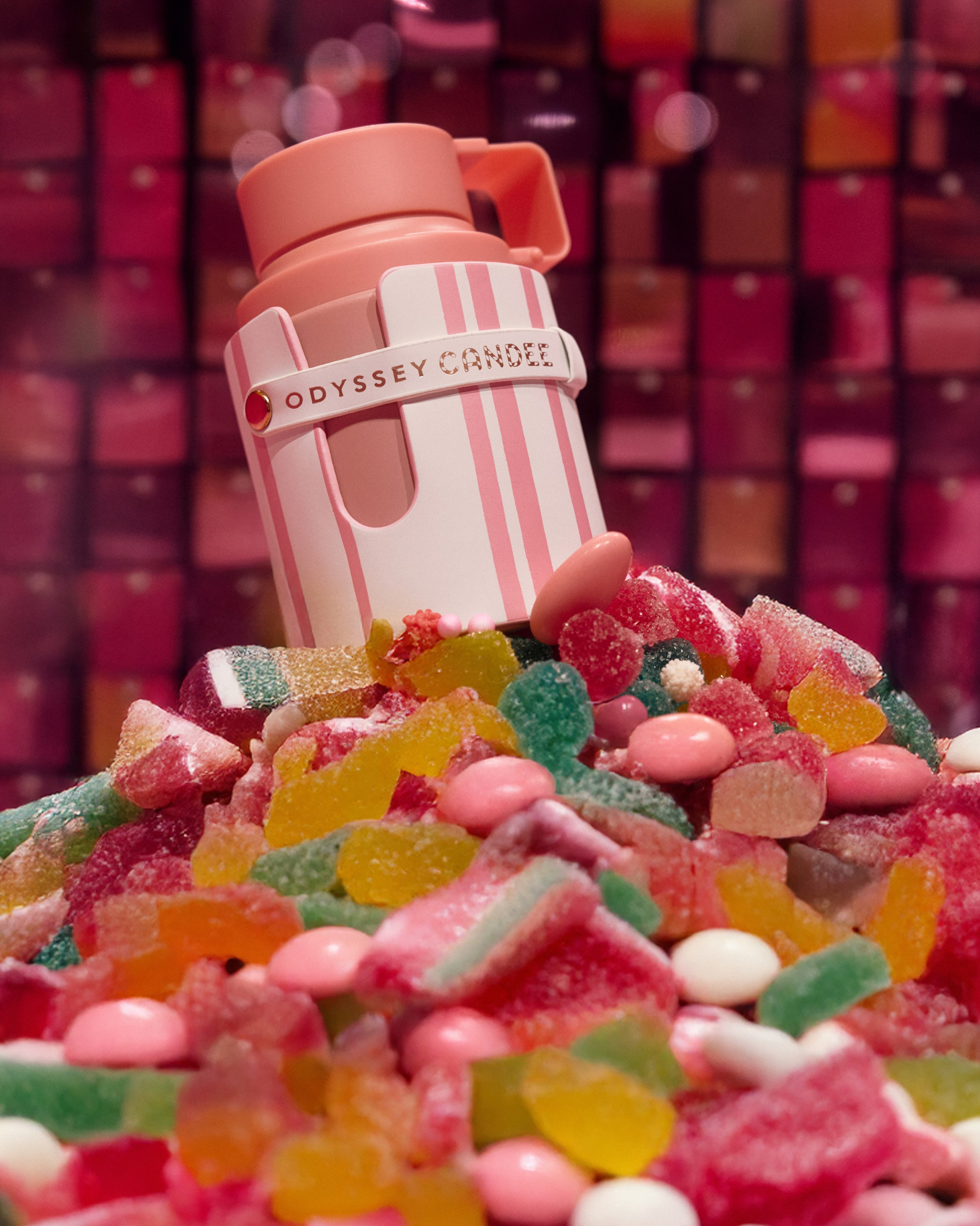 Perfume bottle in pink tones surrounded by bright jelly candies and sweets
