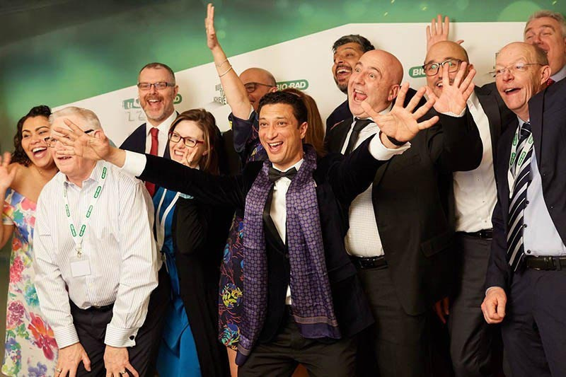 Corporate executives pose for a joyful photo in front of a branding wall during a gala event at the Hilton, Prague.