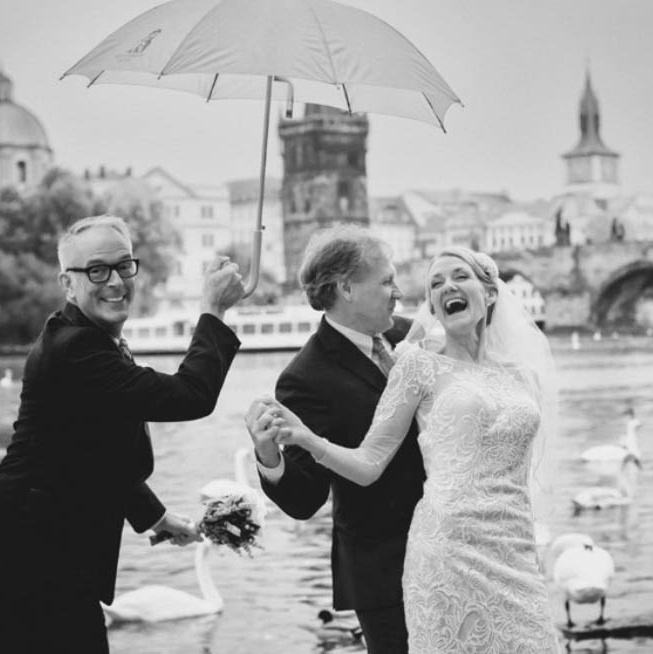 Smiling blonde-haired Swiss bride smiles lovingly towards her Italian groom as he looks towards the camera at a garden in Prague. 