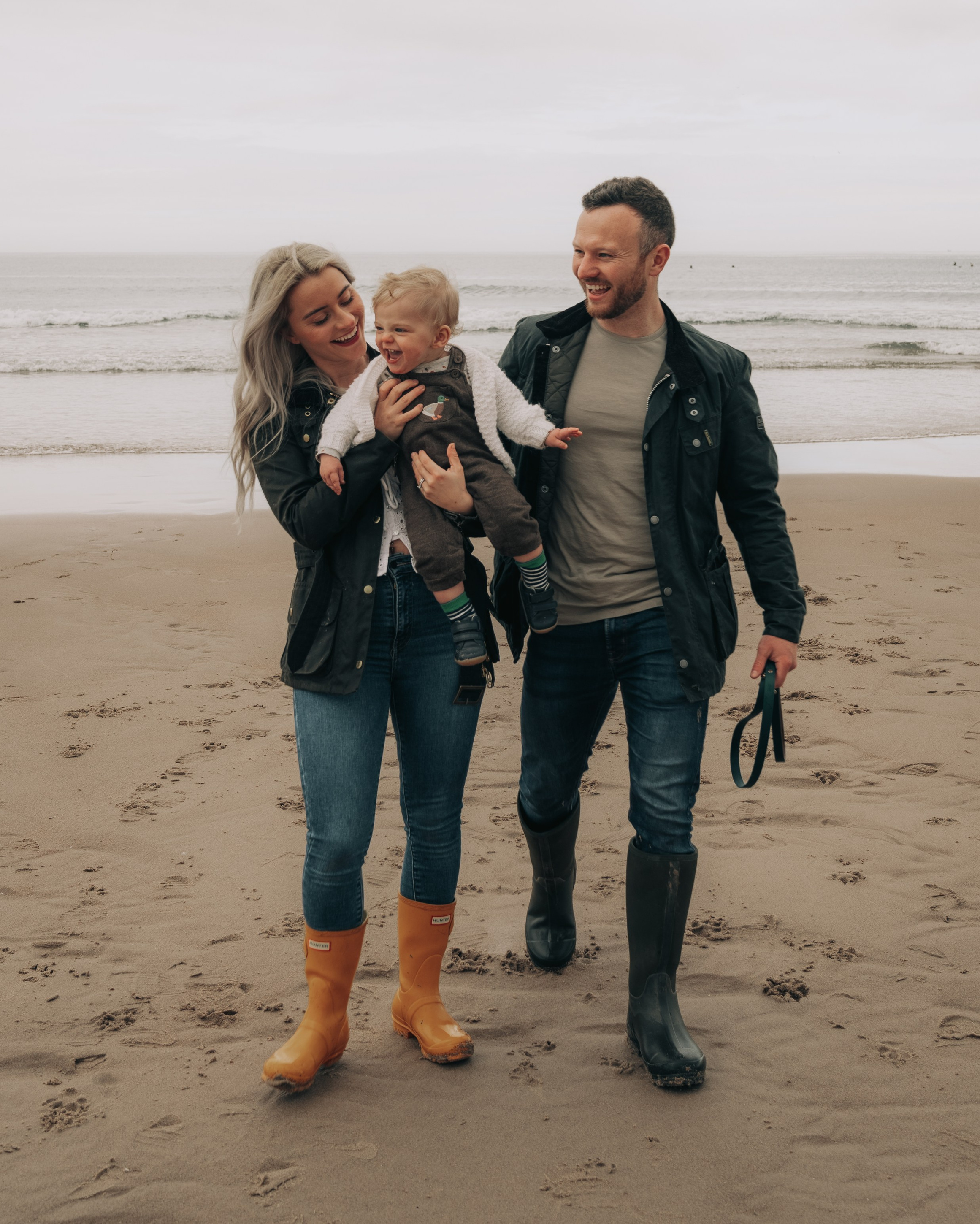 Family walking along the beach with their toddler during a relaxed family photography session in Newcastle upon Tyne.