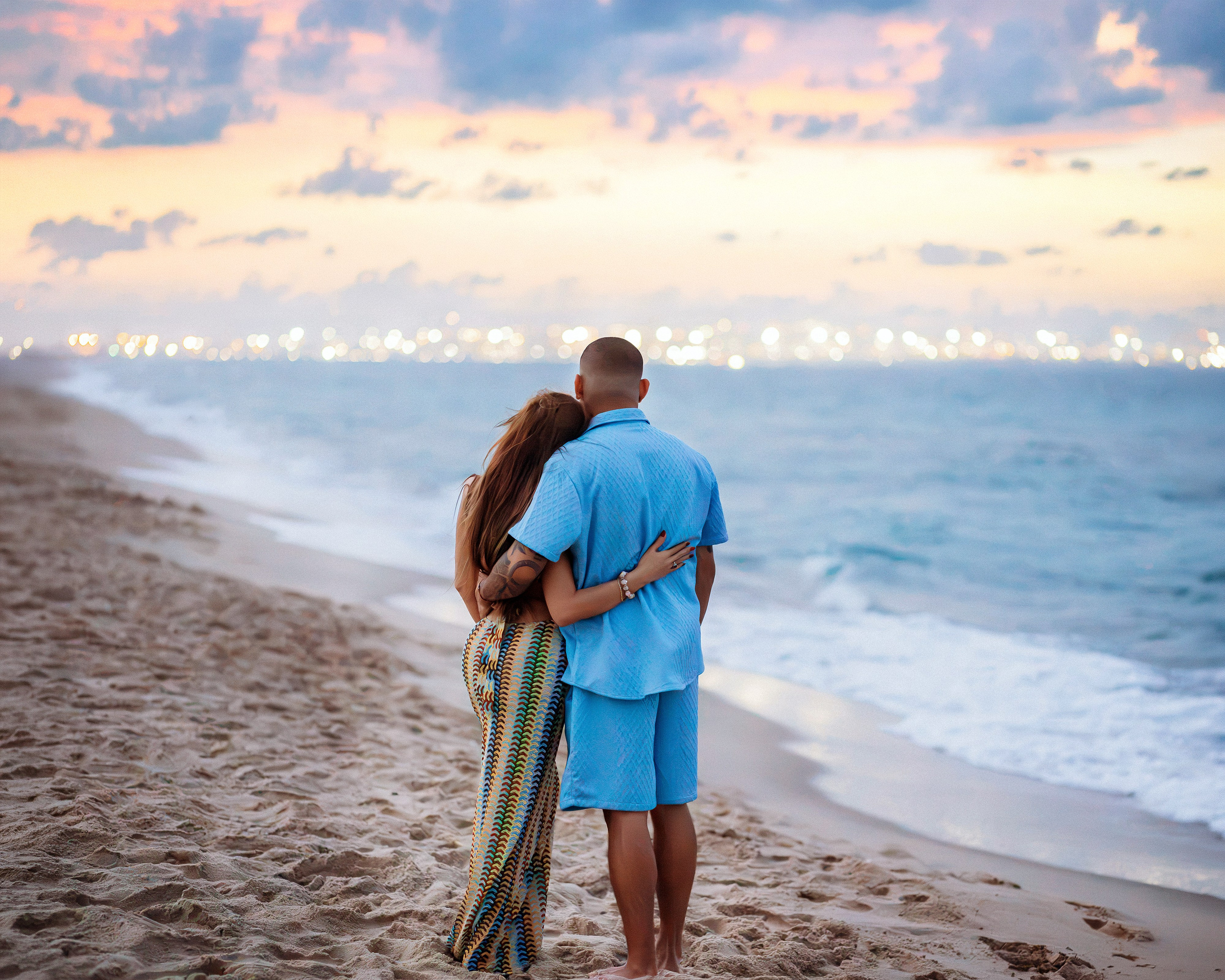 Couple embracing at the water’s edge beneath a pink evening sky during a beach proposal photoshoot in Valencia.