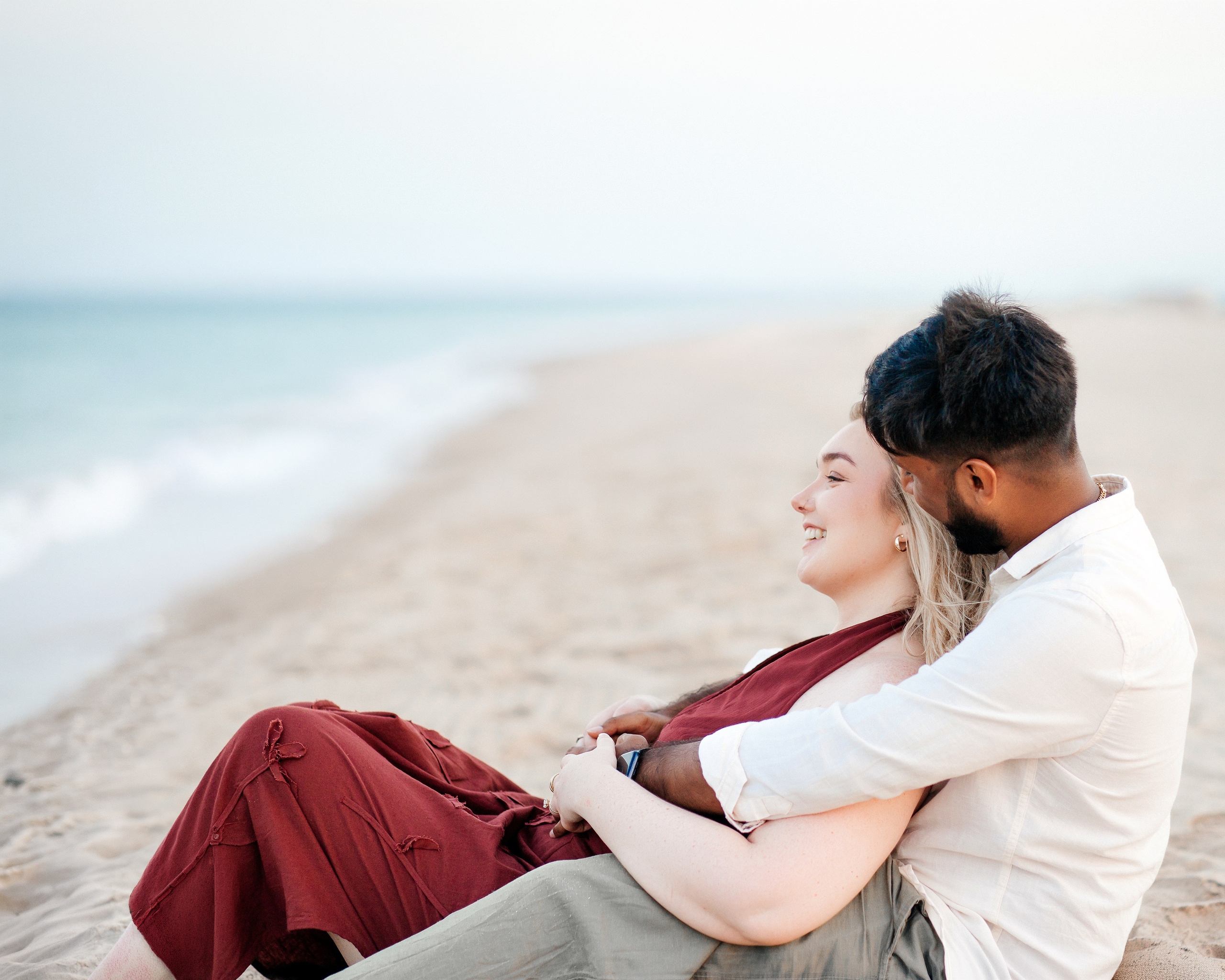 Romantic beach portrait of a couple sitting together by the sea during a proposal photoshoot in Valencia.