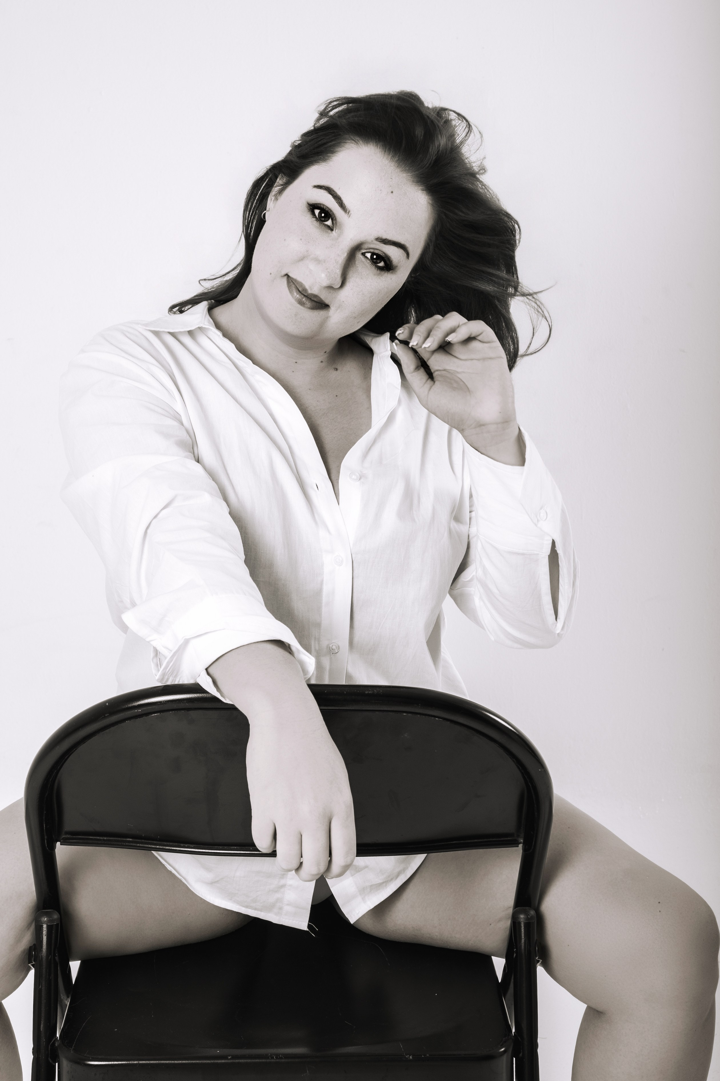 Mujer sentada al revés en una silla con camisa blanca, retrato boudoir en blanco y negro