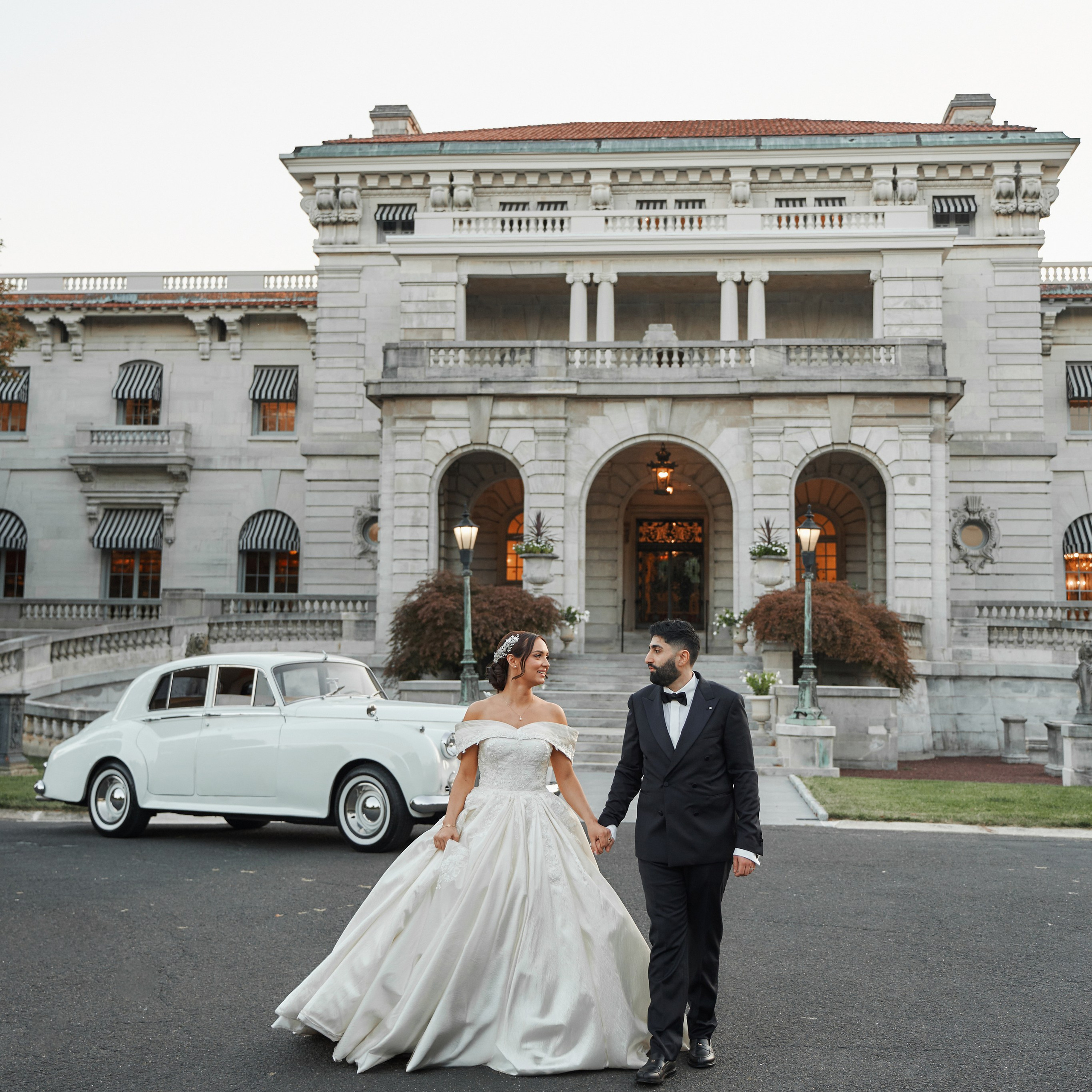 Elegant wedding photo of bride and groom in front of historic mansion with vintage car in New York