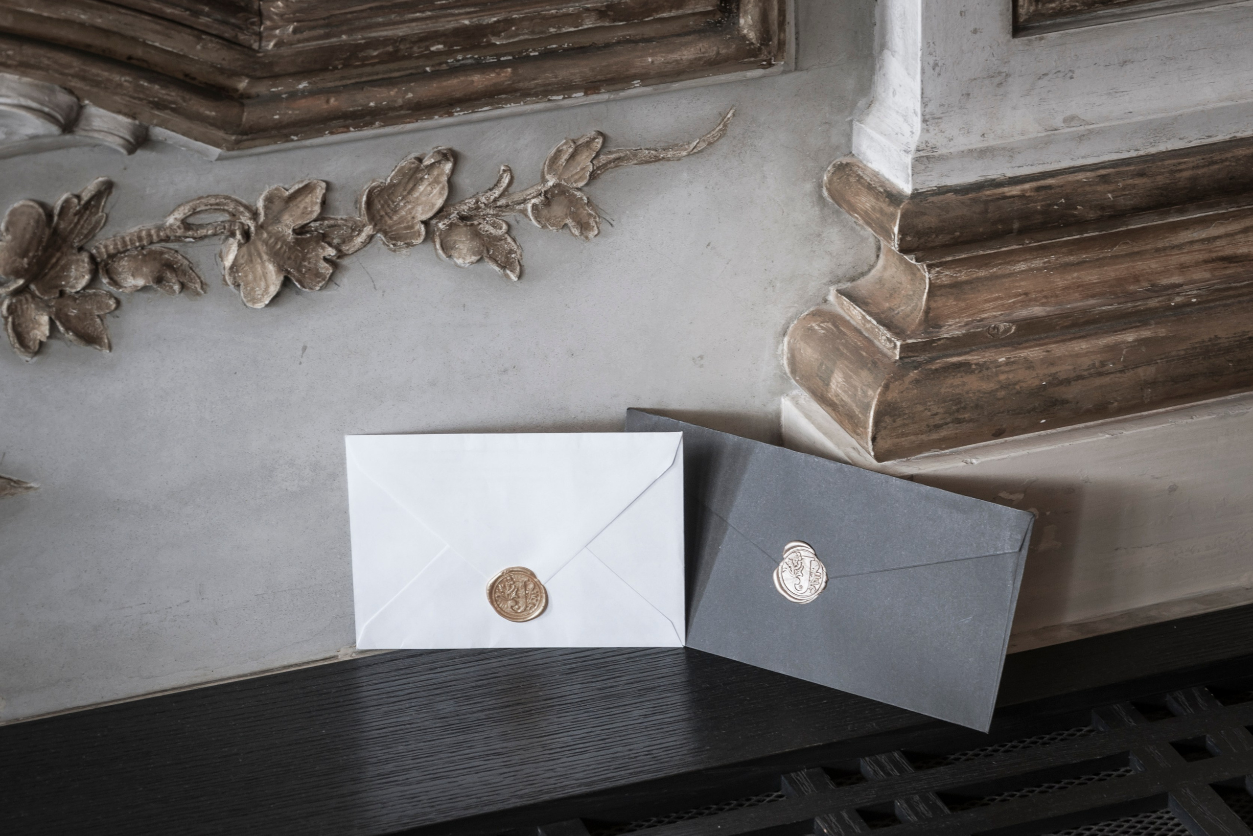 Two luxurious envelopes sealed in golden wax and held in front of a fancy golden ceiling of a palace. 
