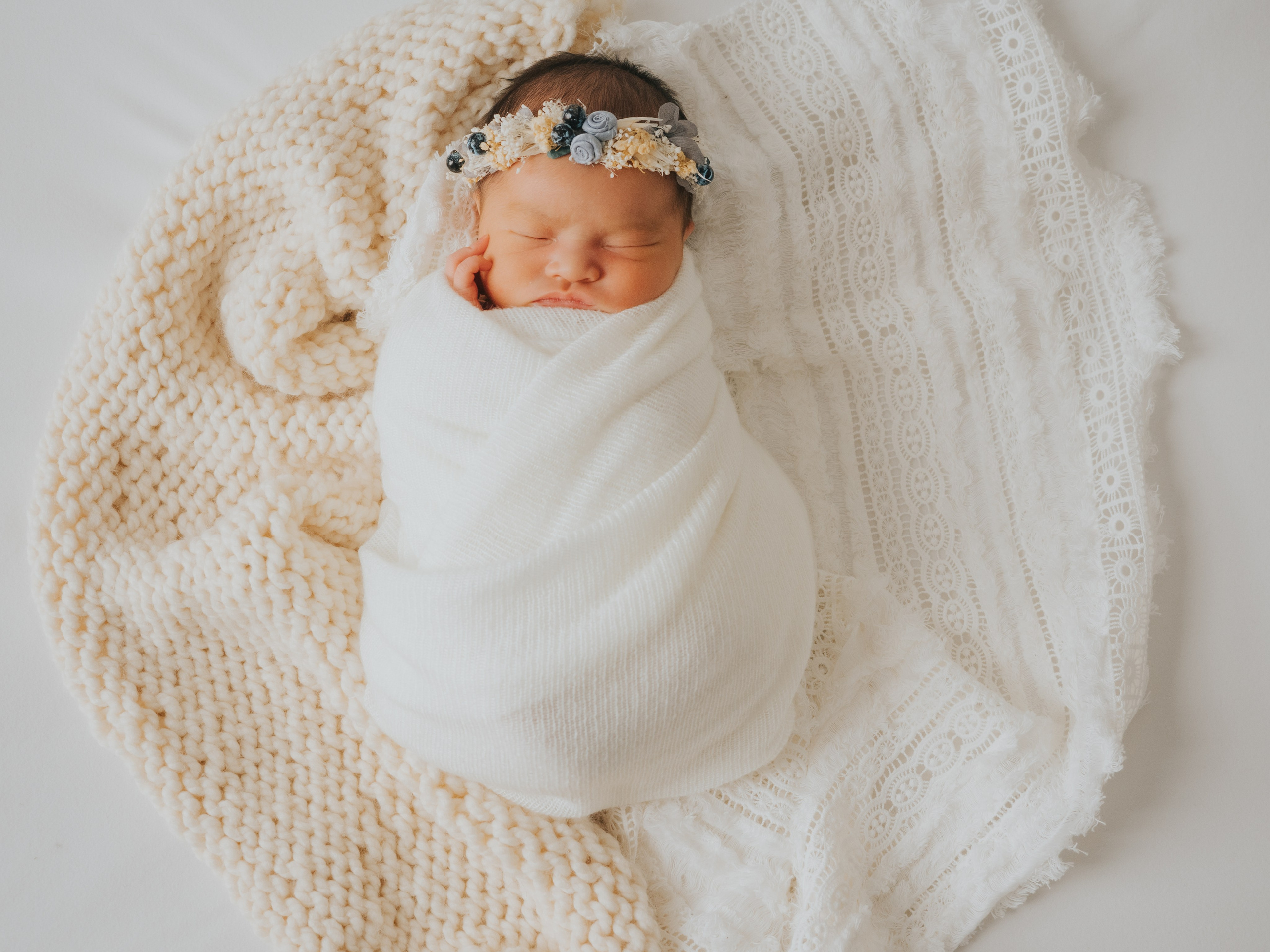 Sleeping baby swaddled on white and cream blankets.