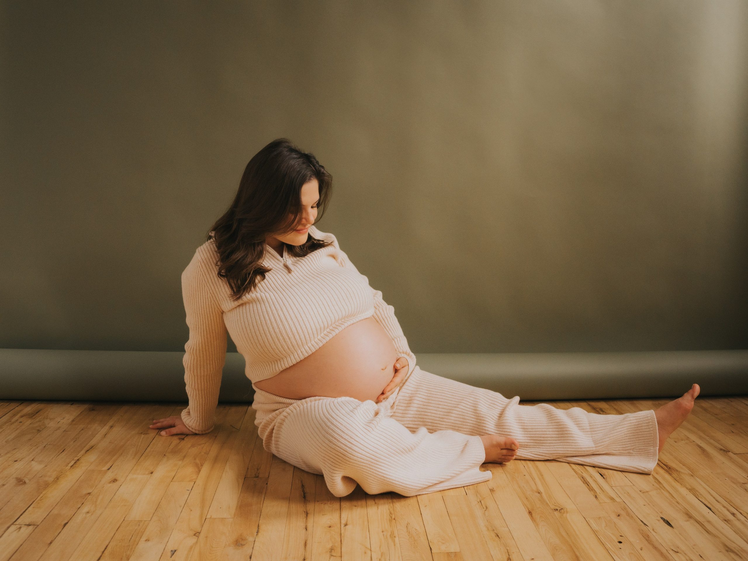 Pregnant woman sitting on floor in Montreal Studio with an olive background.