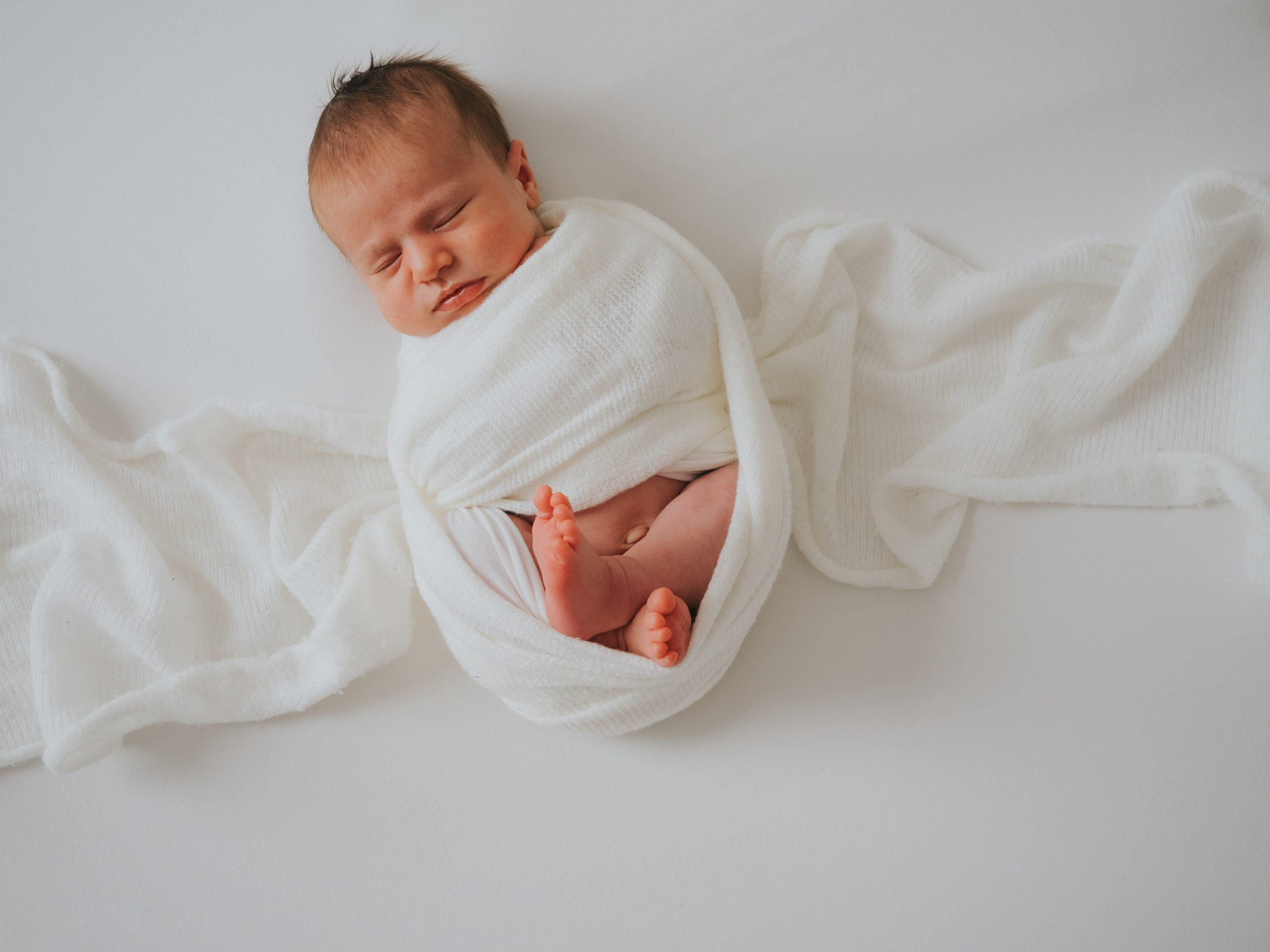 Sleeping newborn swaddled in white blankets