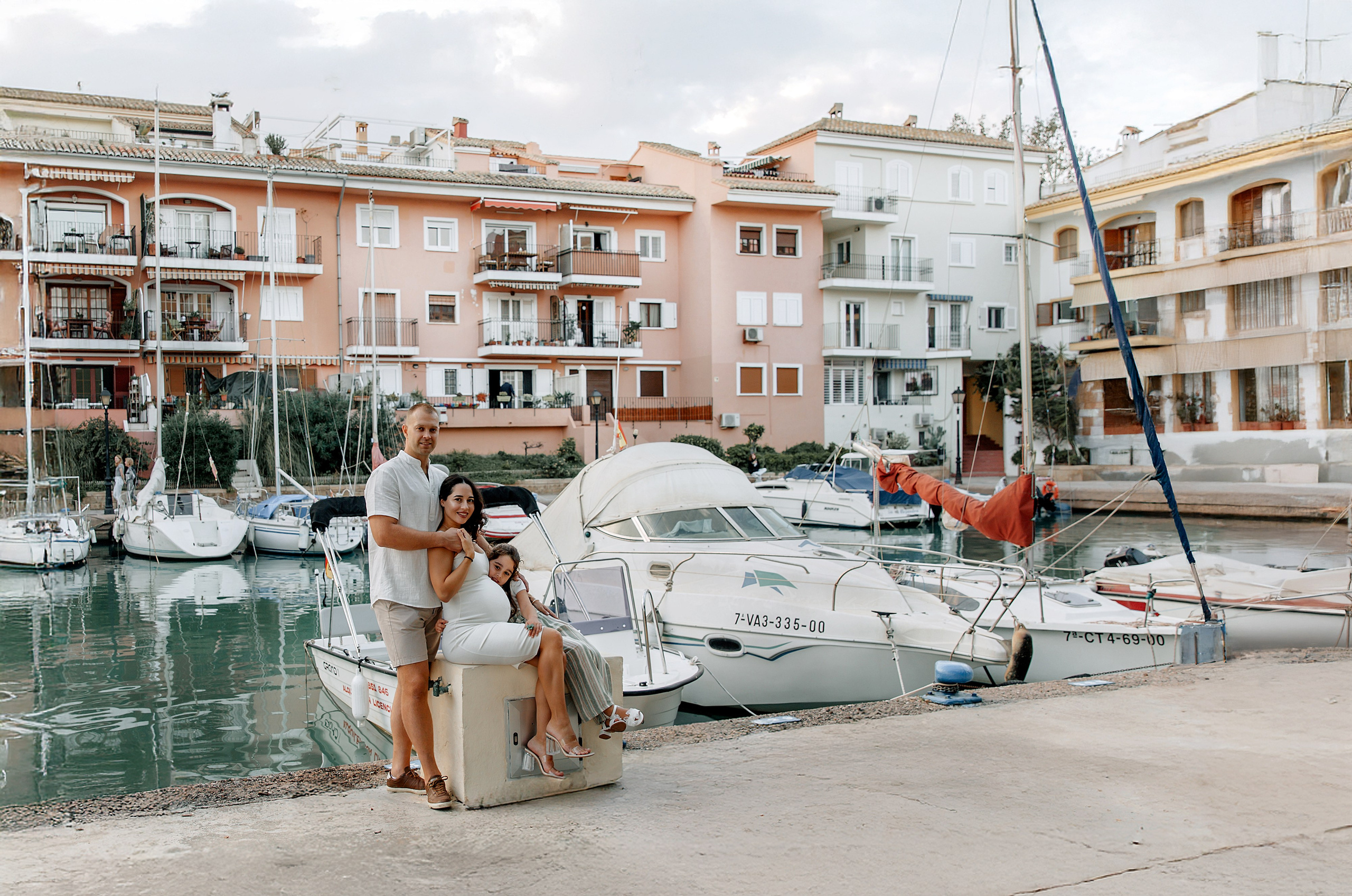 Семейная фотосессия в Порт-Саплая рядом с Валенсией, Испания, с мариной, лодками и яркими зданиями.