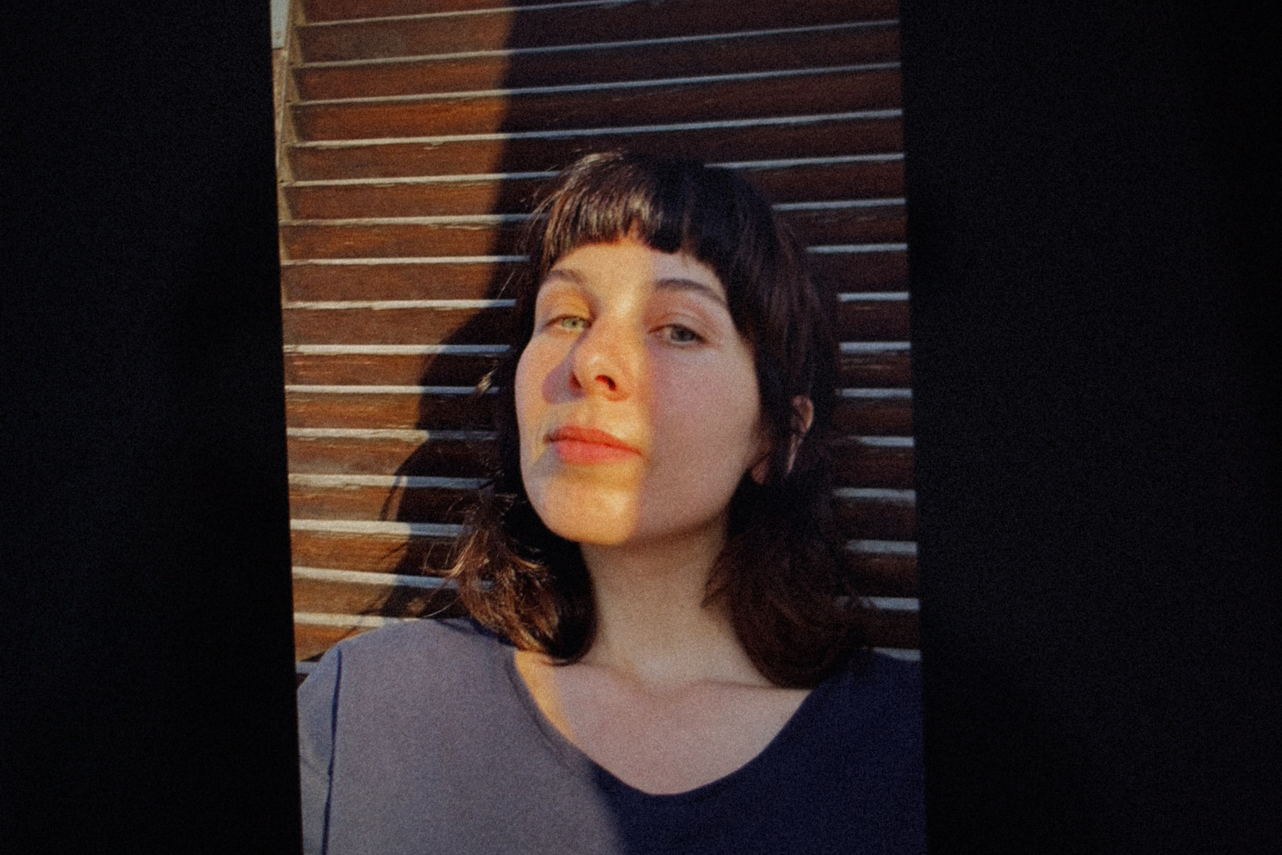A dramatic portrait of a woman standing against a wooden door, with strong contrasting light highlighting her face and features