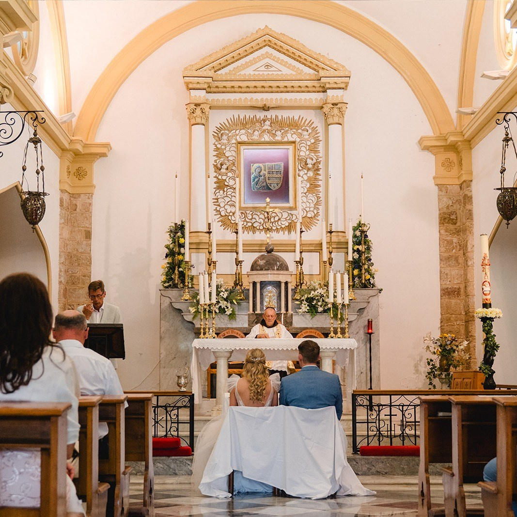 "Festliche Tischdekoration für eine Hochzeit: Blumengesteck mit orangefarbenen Rosen, Pampasgras und Eukalyptus neben einer Tischnummer aus Glas."