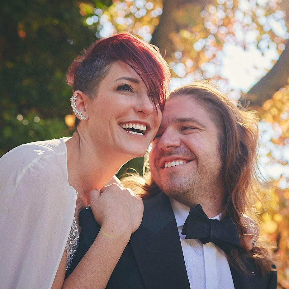 Red-haired bride holding her flowing veil aloft smiles seductively to her bouquet holding groom as he leans back against a railing in appreciation at the Vrtba Garden in Prague. 