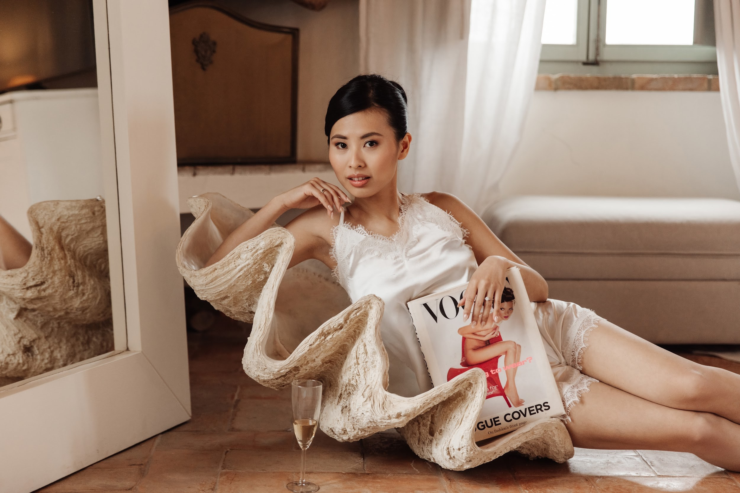 Bride putting on earrings during wedding morning preparation by the window