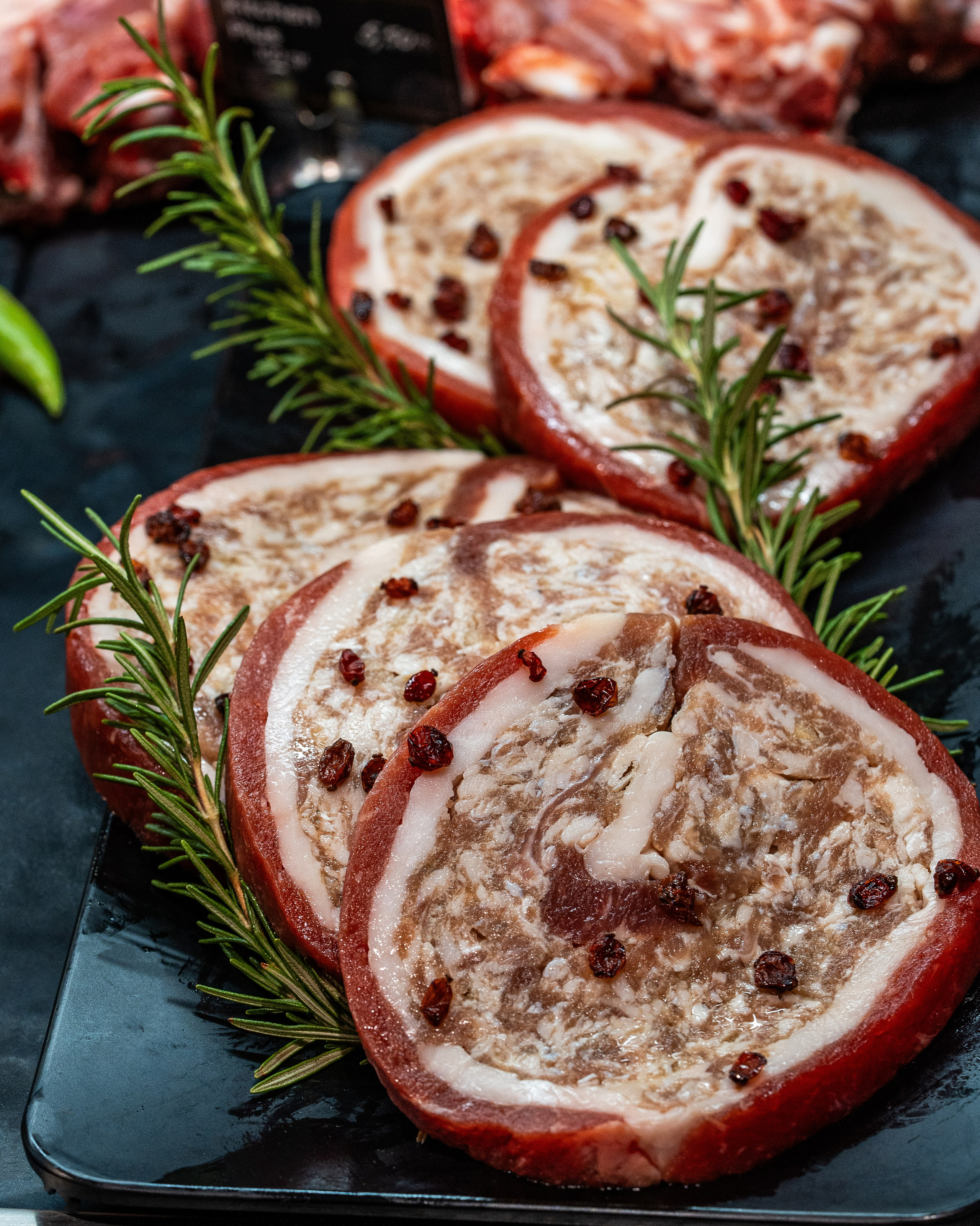 Qara, parlaq tepsidə rozmarin budaqları ilə bəzədilmiş və üzərində qırmızı dənələr (ehtimal ki, qarağat və ya istiot) olan dörd dilim döş əti rulonu (mal və ya quzu).