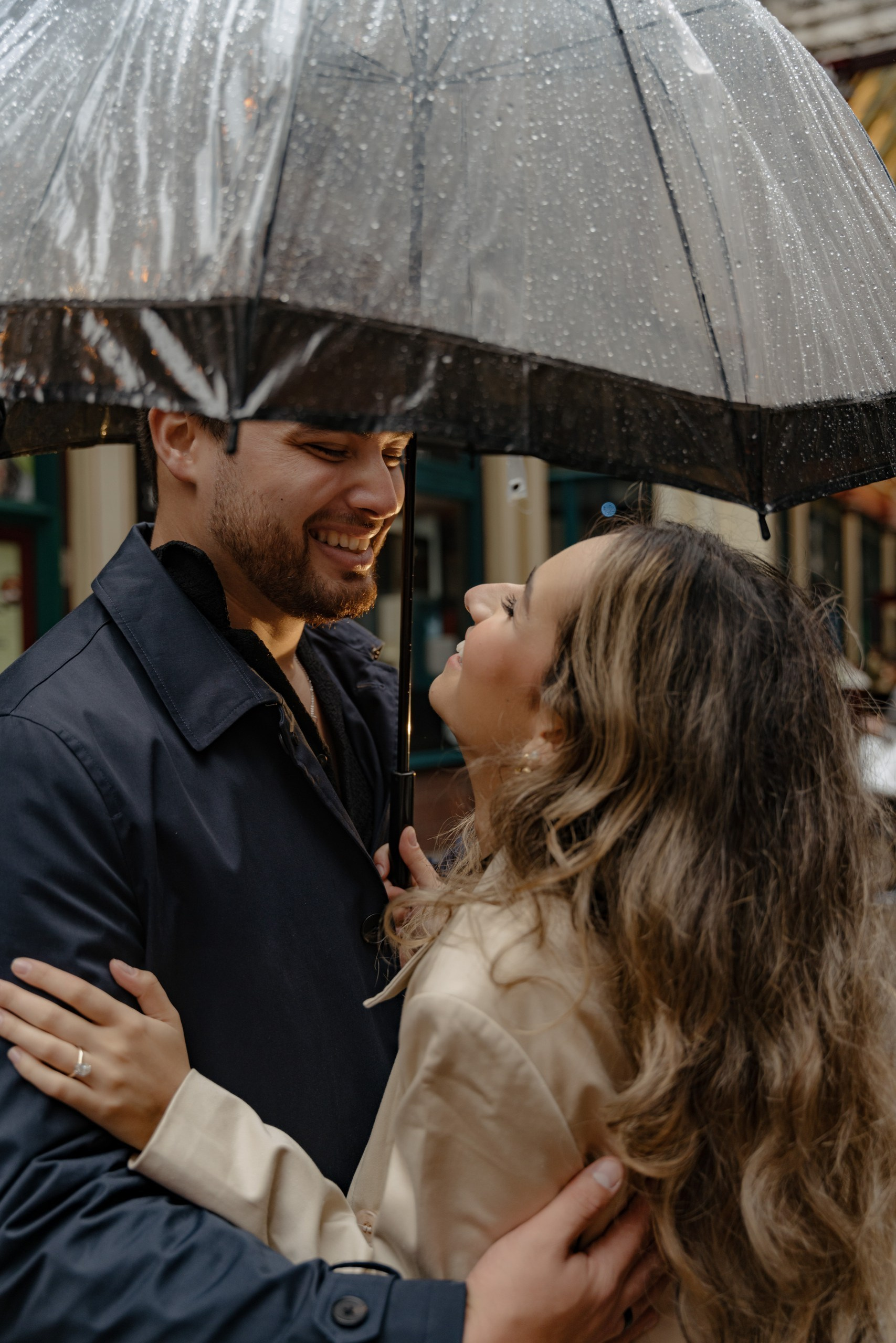 Romantic couple portrait in London rain with umbrella and soft cinematic city light.