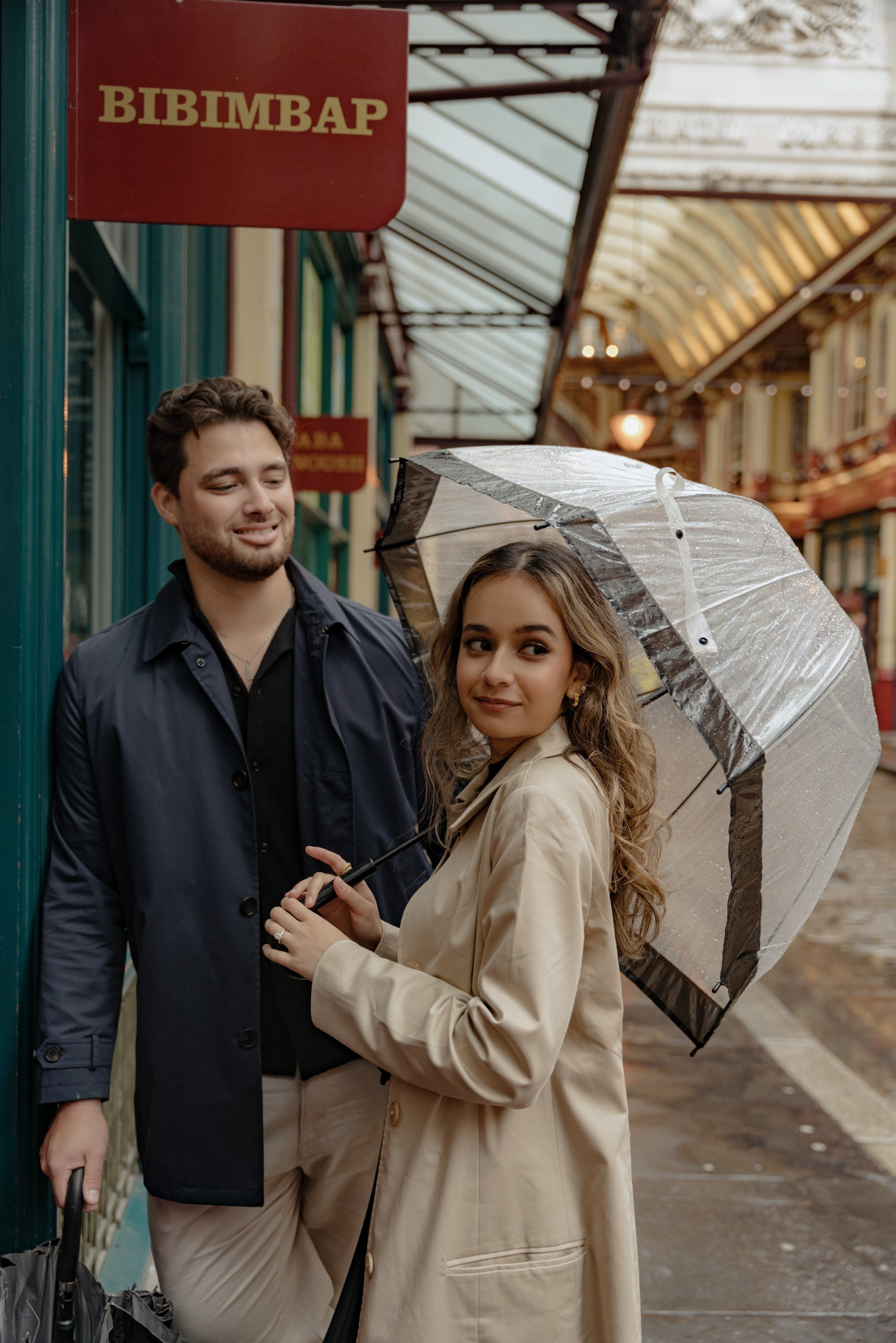 Couple under umbrella during rainy London photoshoot in elegant neutral outfits.